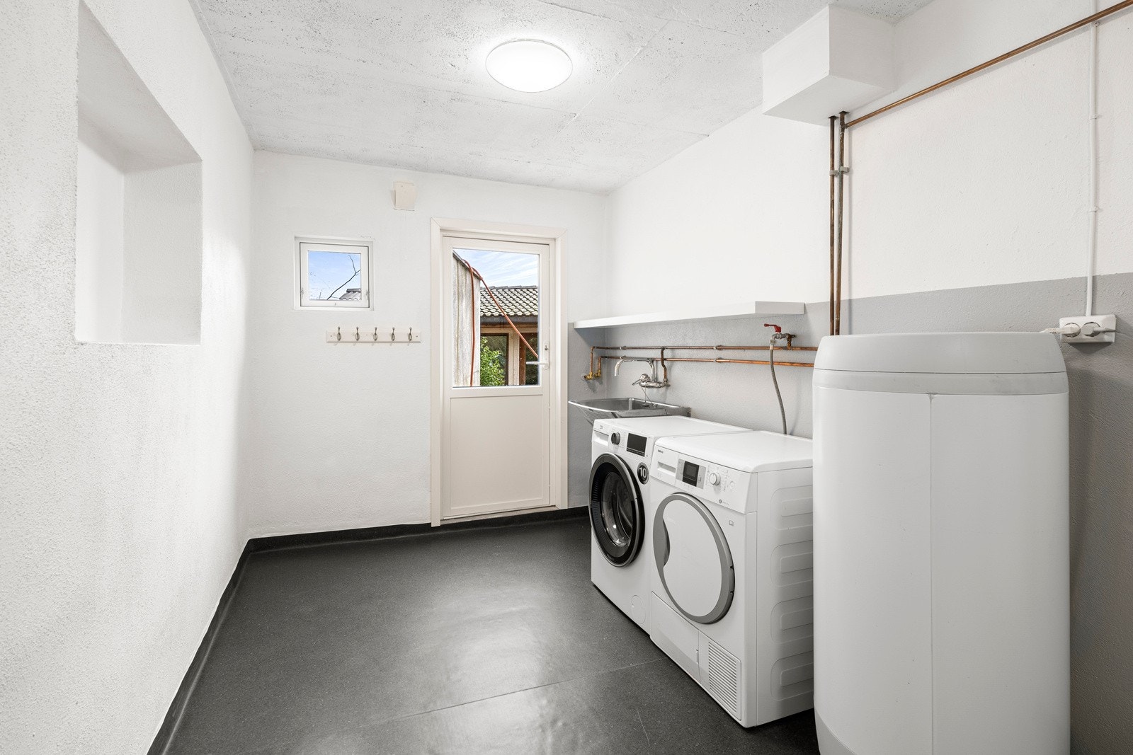 Vaskerommet har hylleløsninger, sluk, varmtvannsbereder og opplegg for vaskemaskin. Rommet har også egen utgang til hagen, noe som kan være ekstra praktisk for blant annet dyreeiere. Galleribilde