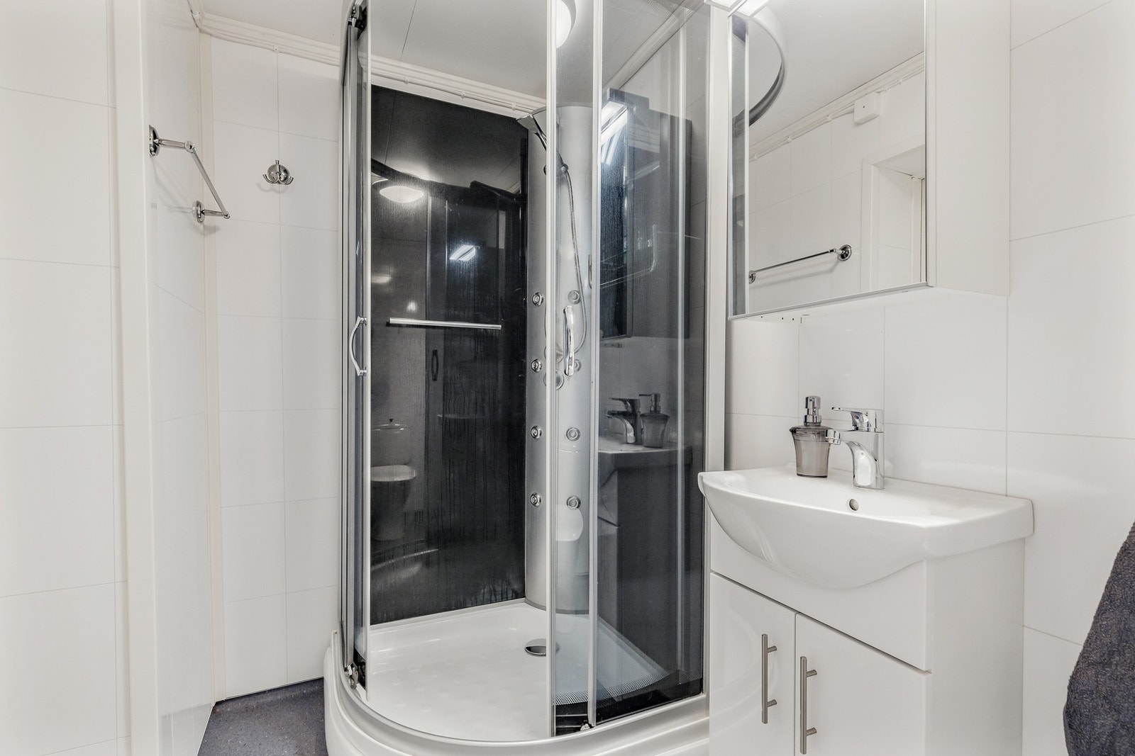 Rommet er innredet med gulvstående toalett, dusjkabinett og vegghengt servantskap og speilskap Galleribilde