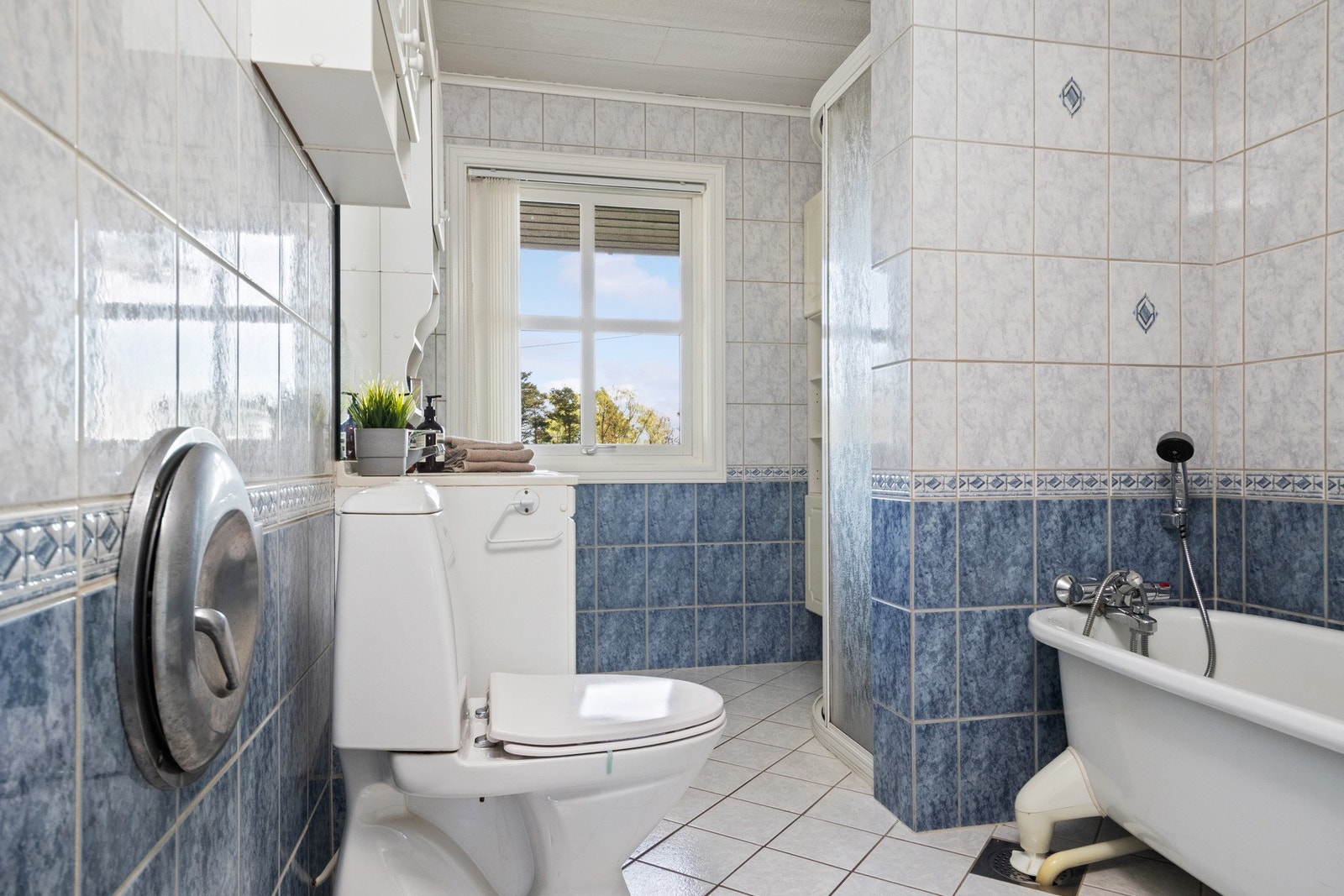 Badet er helfliset i ulike blåtoner, og har både et badekar med dusjløsning og et dusjhjørne med skyvedører. Badet har skittentøysjakt til vaskerommet. Galleribilde