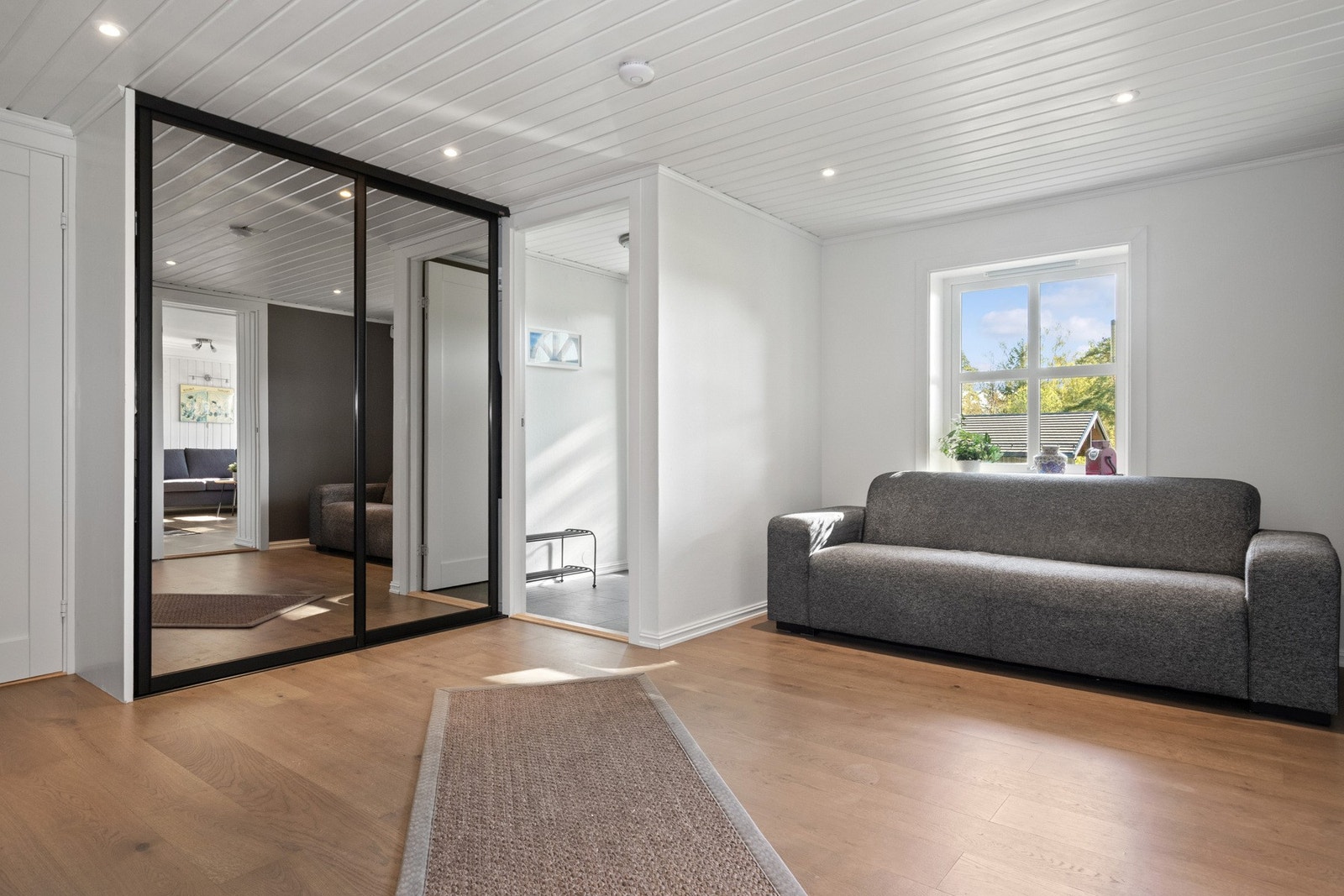 Jakkene ryddes enkelt bort i en stor skyvedørsgarderobe med speilfronter og sort innramming. Galleribilde