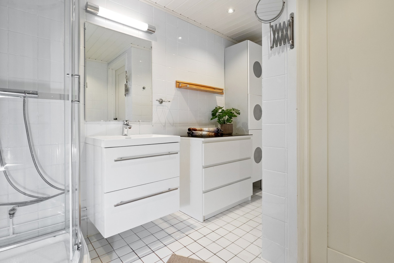 Badet har hvite fliser, og en nyere innredning består av servant med hvite skuffer, et hvitt høyskap og et speil med tilhørende lys. Galleribilde