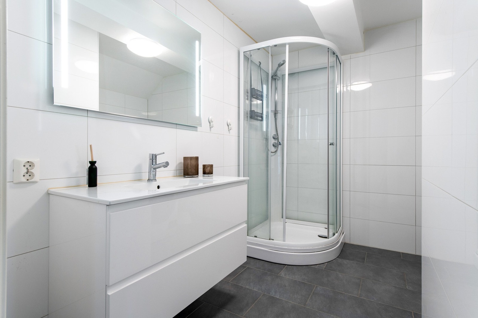 Badet er moderne, etablert i 2019, da hele leiligheten ble renovert. Badet har grå fliser på gulv med gulvvarme, hvite fliser på veggene og hvitmalt, listefri himling. Noen fliser på den ene veggen ble skiftet i 2023. Innredningen består av en heldekkende Galleribilde