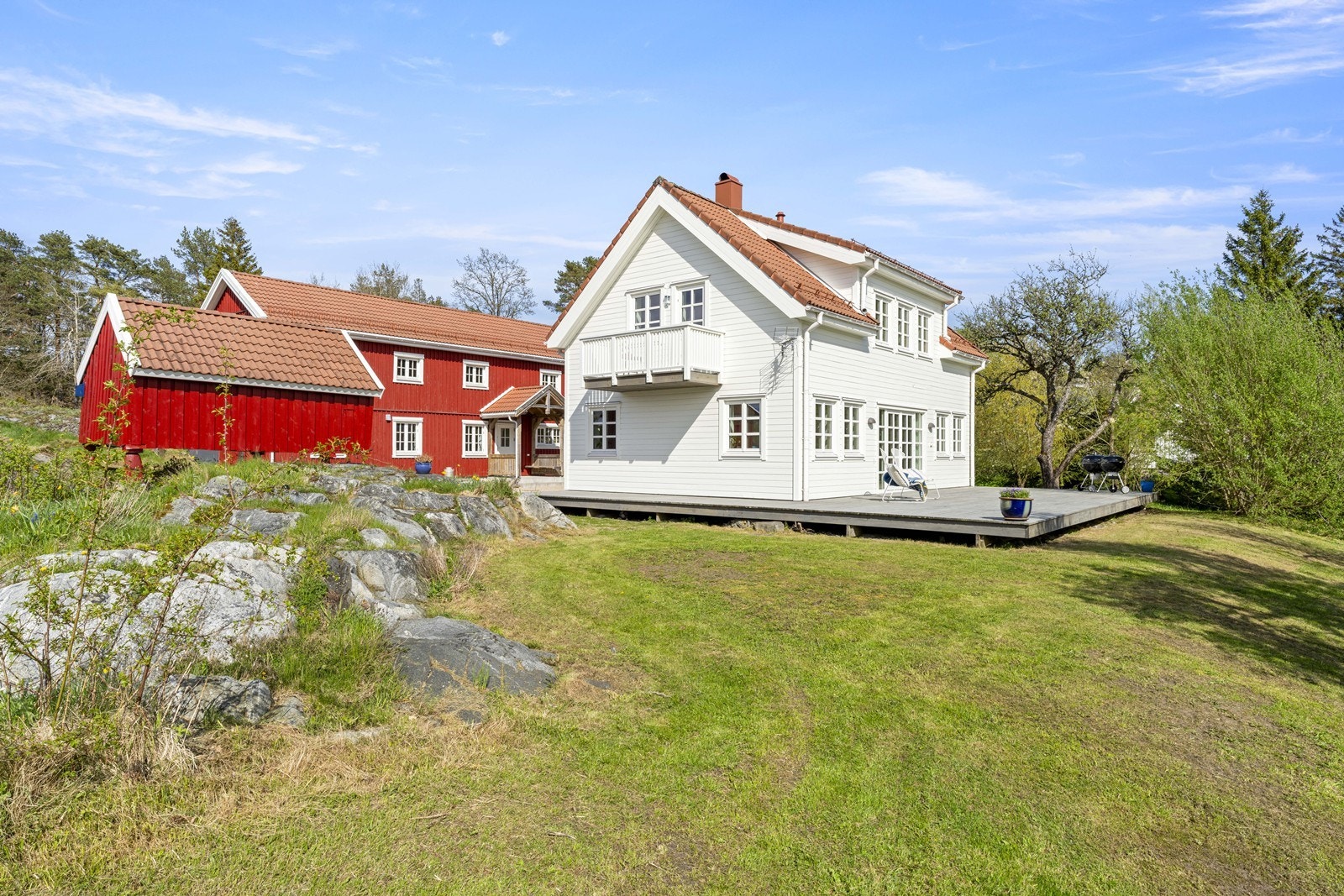Fasadebilde med låven i bakgrunnen. Stor, solrik terrasse på fremsiden Galleribilde