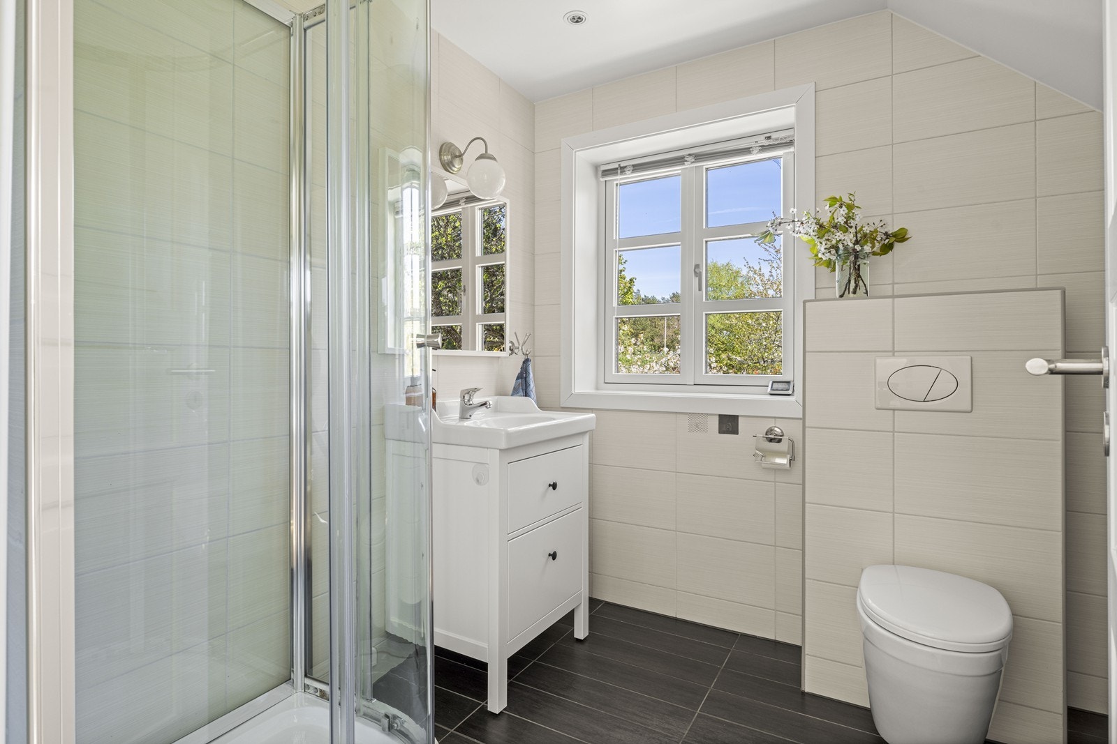 Bad tilhørende hovedsoverommet med fliser på gulv og vegger, dusj, wc og servant med skuffer og speil Galleribilde