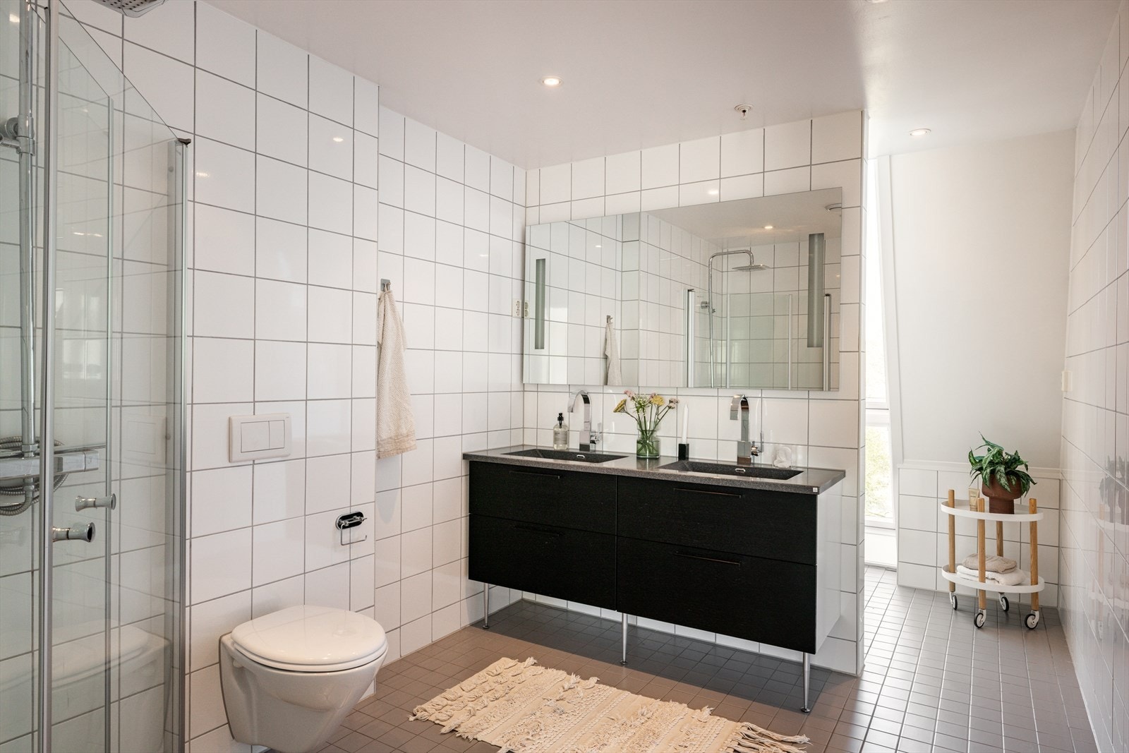 Leiligheten har et meget romslig og svært praktisk innredet baderom som er delt inn i to soner. Badets hovedfasiliteter finner du skjermet i første del av baderommet, videre deler en halvvegg av til det lyse, praktiske vaskerommet. Galleribilde