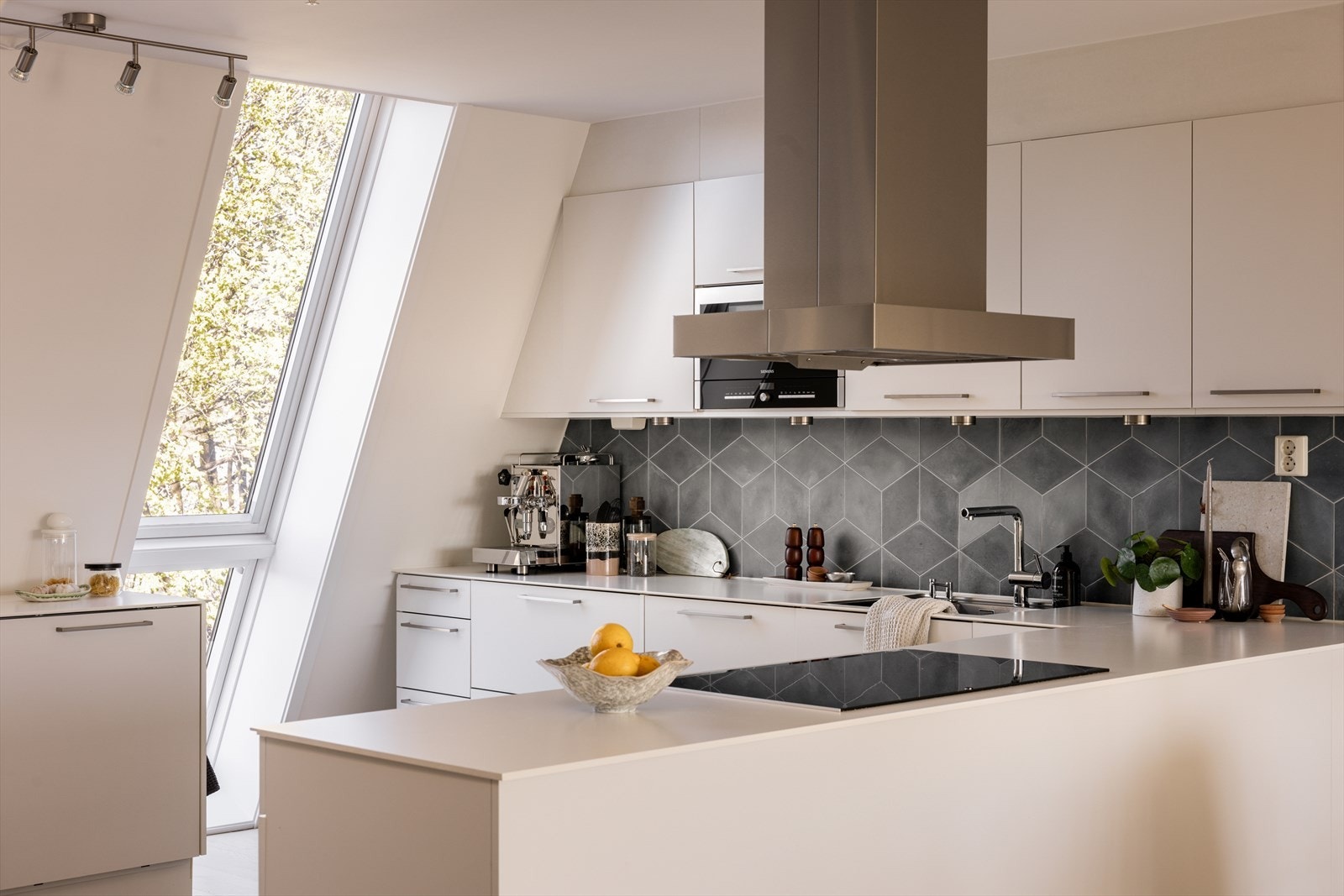 Kjøkkenets utforming gir god arbeidsplass. Legg merke til det fantastiske vinduet som både gir lys i rommet samtidig som det fungerer som et kult design med sin skrå utforming fra gulv til tak. Galleribilde