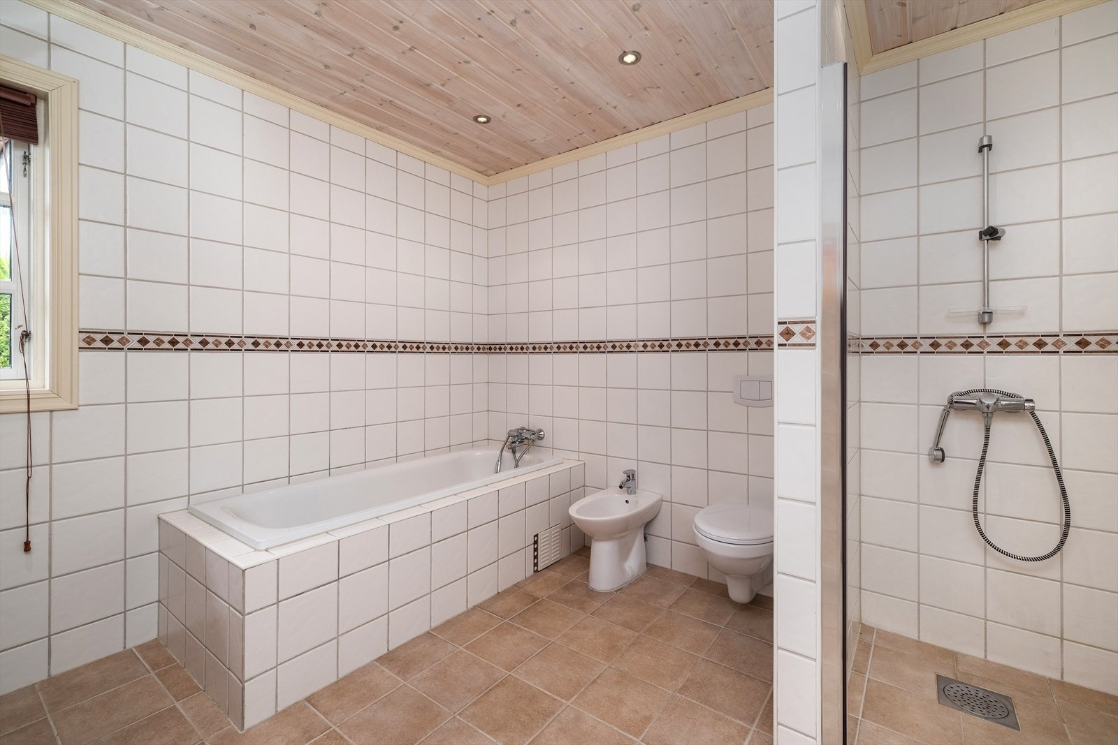 Badet inneholder servantinnredning med speil og høyskap, dusjnisje, innmurt badekar, bide og toalett. Galleribilde