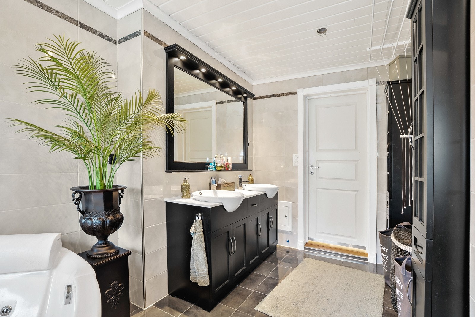 Den sorte innredningen har profilerte skapfronter, to nedfelte servanter og et stort speil med belysning i overkant. Galleribilde