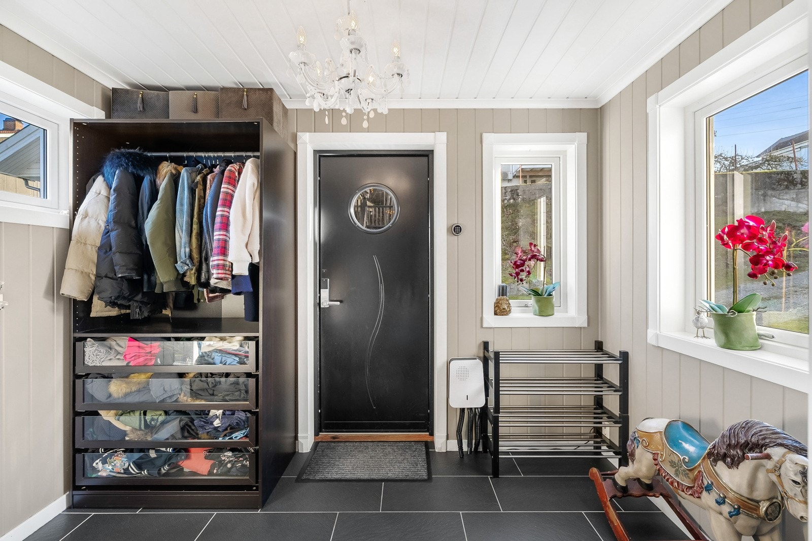 Eneboligen har inngang til en pen entré med sorte fliser over gulv med varme, veggpanel malt i en harmonisk naturtone, sort inngangsdør og naturlig lys fra tre sider. Galleribilde