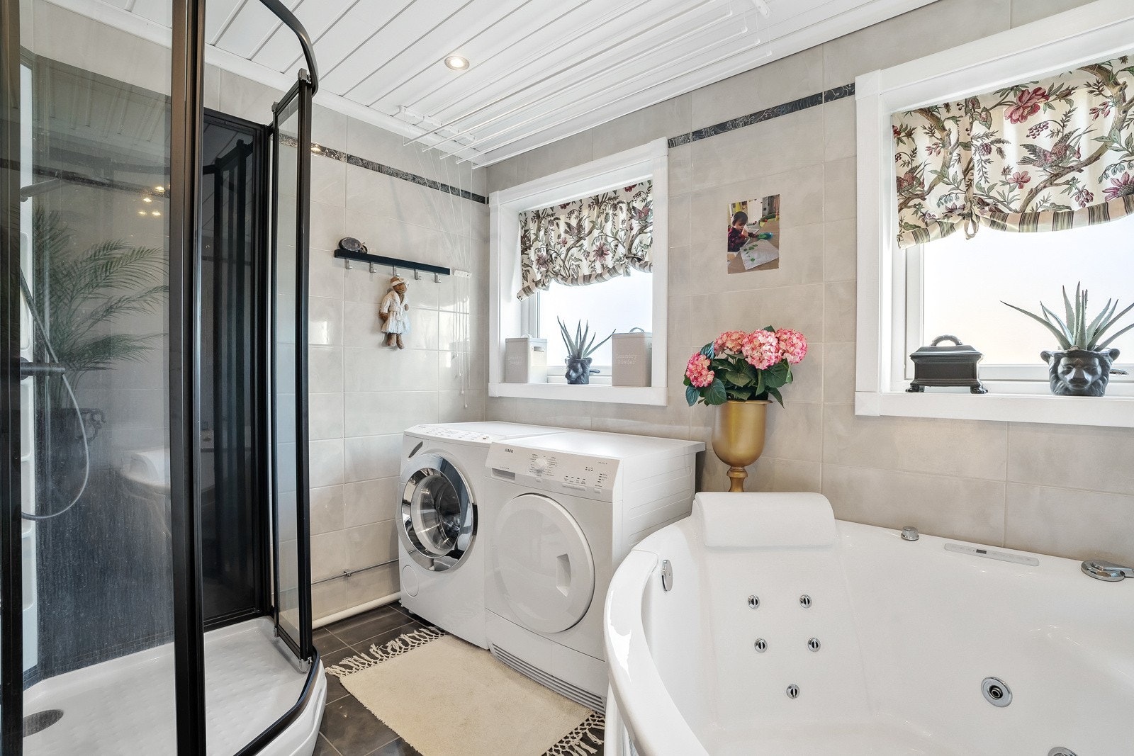 Videre har badet både stort dusjkabinett med sorte detaljer, et deilig hjørnebadekar og opplegg for vaskemaskin. Galleribilde