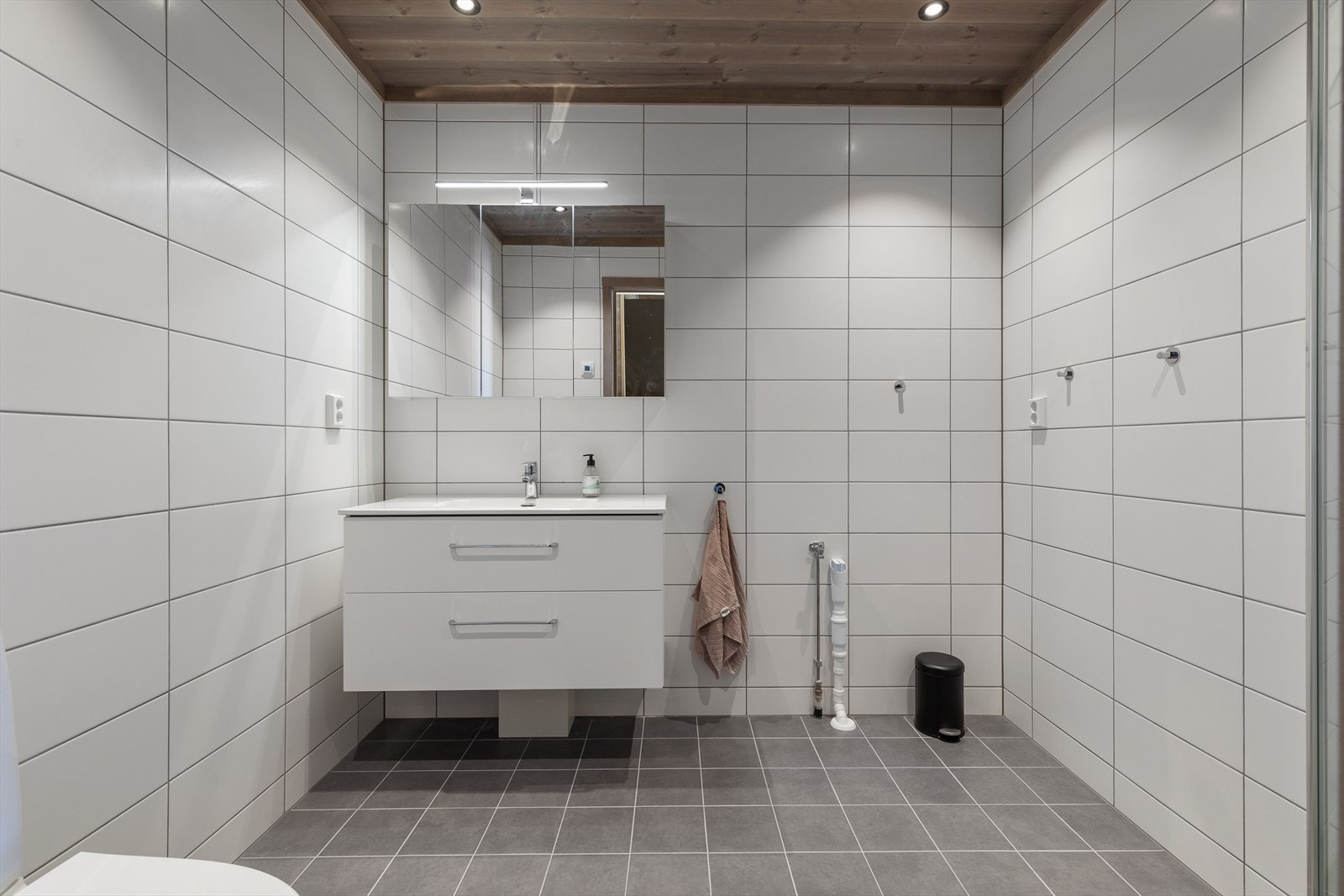 Badet er helfliset med varmekabler i gulv. Rommet har innredning med nedfelt servant, toalett, dusjvegger/hjørne og opplegg for vaskemaskin. Galleribilde