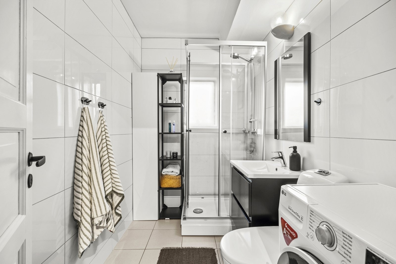 Flislagt bad med varmekabler i gulv. Badet er bestående av gulvstående klosett, dusjkabinett og servant i helstøpt plate og belysning over. Galleribilde