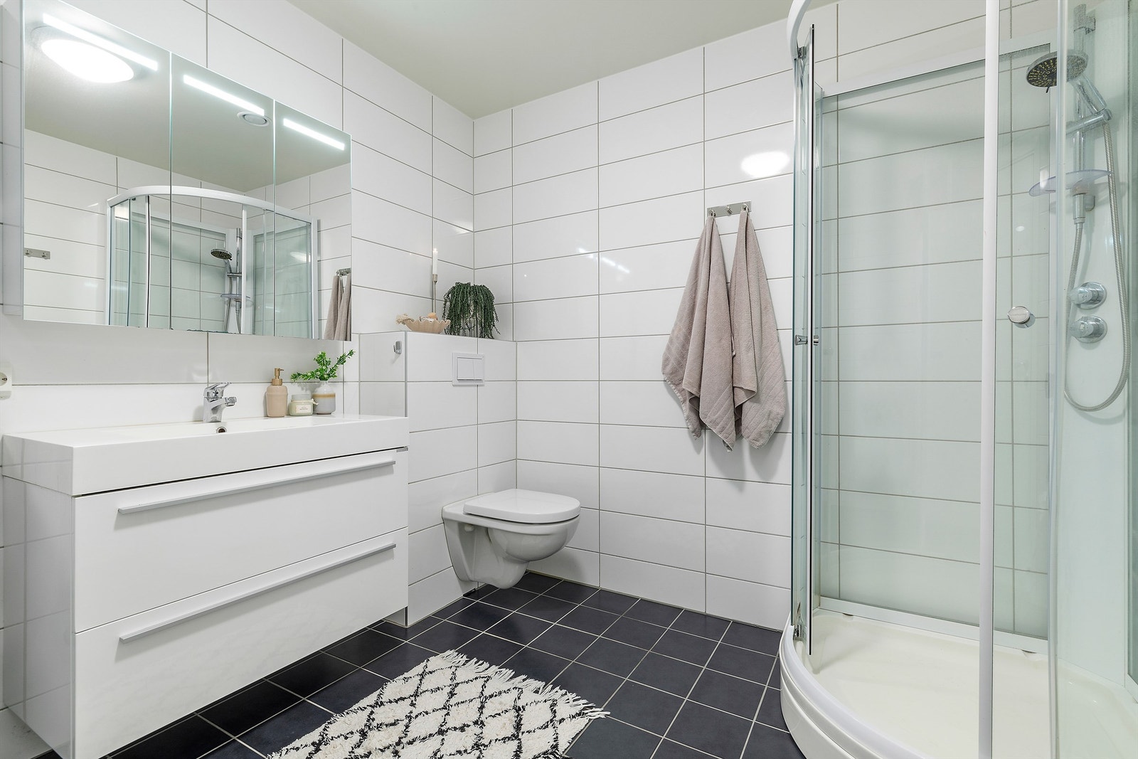 Flott flislagt bad på 7m². Mekanisk avtrekk med ventil i himling. Godt med oppbevaring i dobbelskuffeseksjon og vegghengt speilskap med overlys og stikkontakt Galleribilde