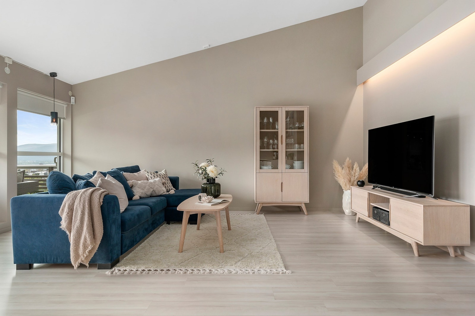 Rommet har en gjennomført, moderne stil med lyse gulv, dempede jordtoner på veggene og store vindusflater som slipper inn rikelig med naturlig lys og gir en fantastisk utsikt! Legg og merke til den flotte lyslist-detaljen over tv! Galleribilde