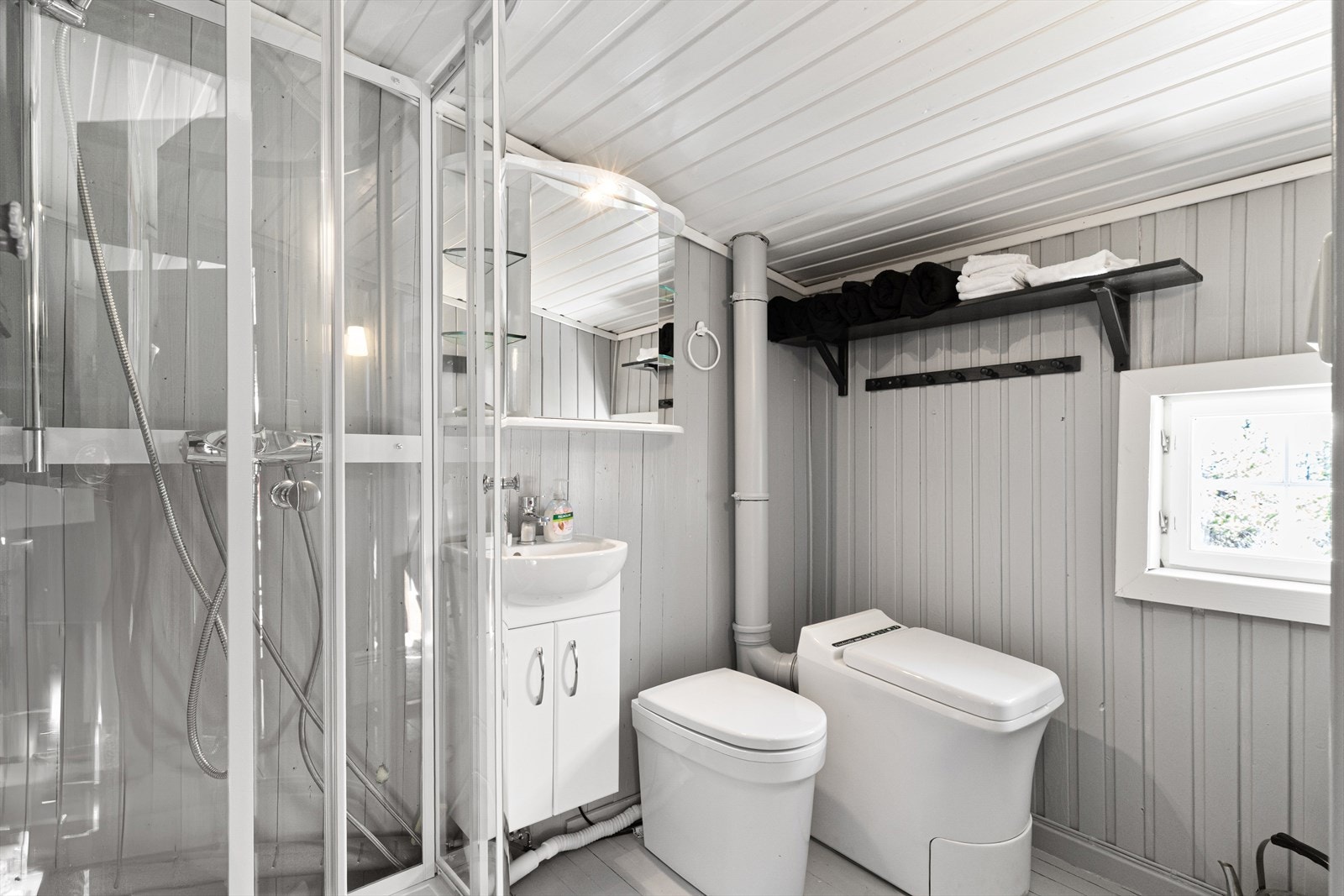 Badet er malt i en lekker lys gråblå farge. Det er montert forbrenningstoalett og urinal på badet, samt et dusjkabinett og en servant med underskap. Galleribilde