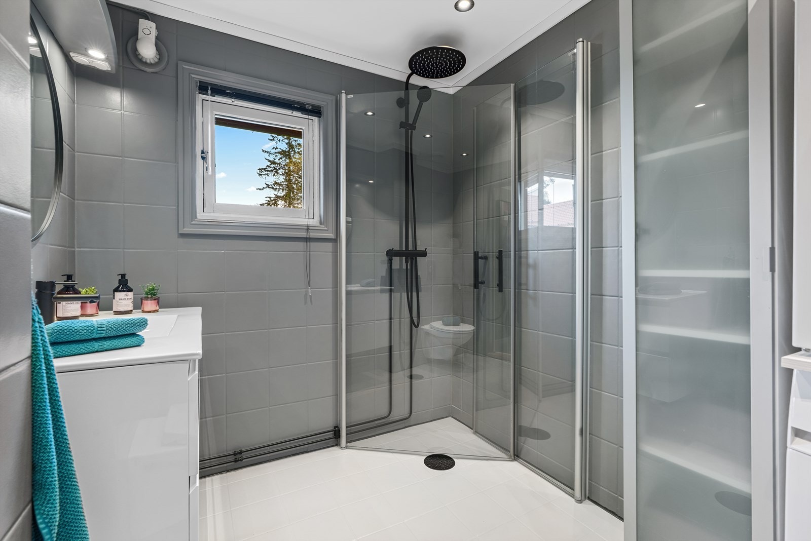 Rekkehuset har et pent utbygd bad. Badet har benkeskap med glatte fronter, servant i helstøpt plate (2023), og dusj på gulv med dører i herdet glass. Galleribilde