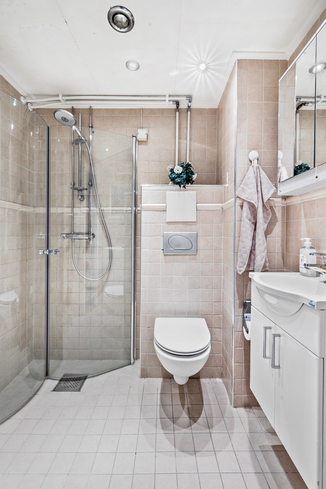 Flislagt bad med benkeskap av glatte fronter og dusj på gulv med dører i herdet glass. Galleribilde