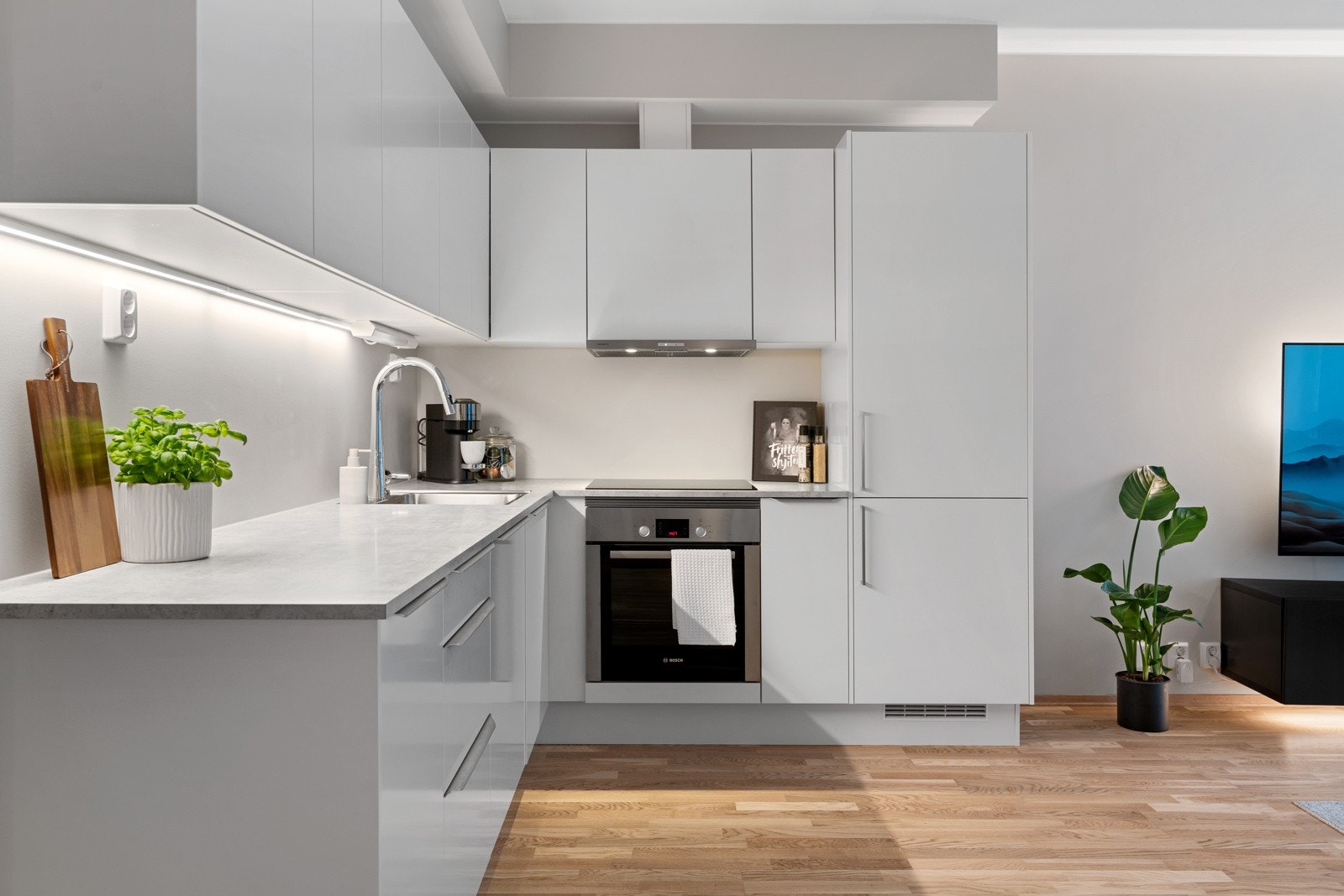 Leilighetens kjøkken har en tidløs og elegant utforming, med hvite fronter og integrerte hvitevarer. Galleribilde