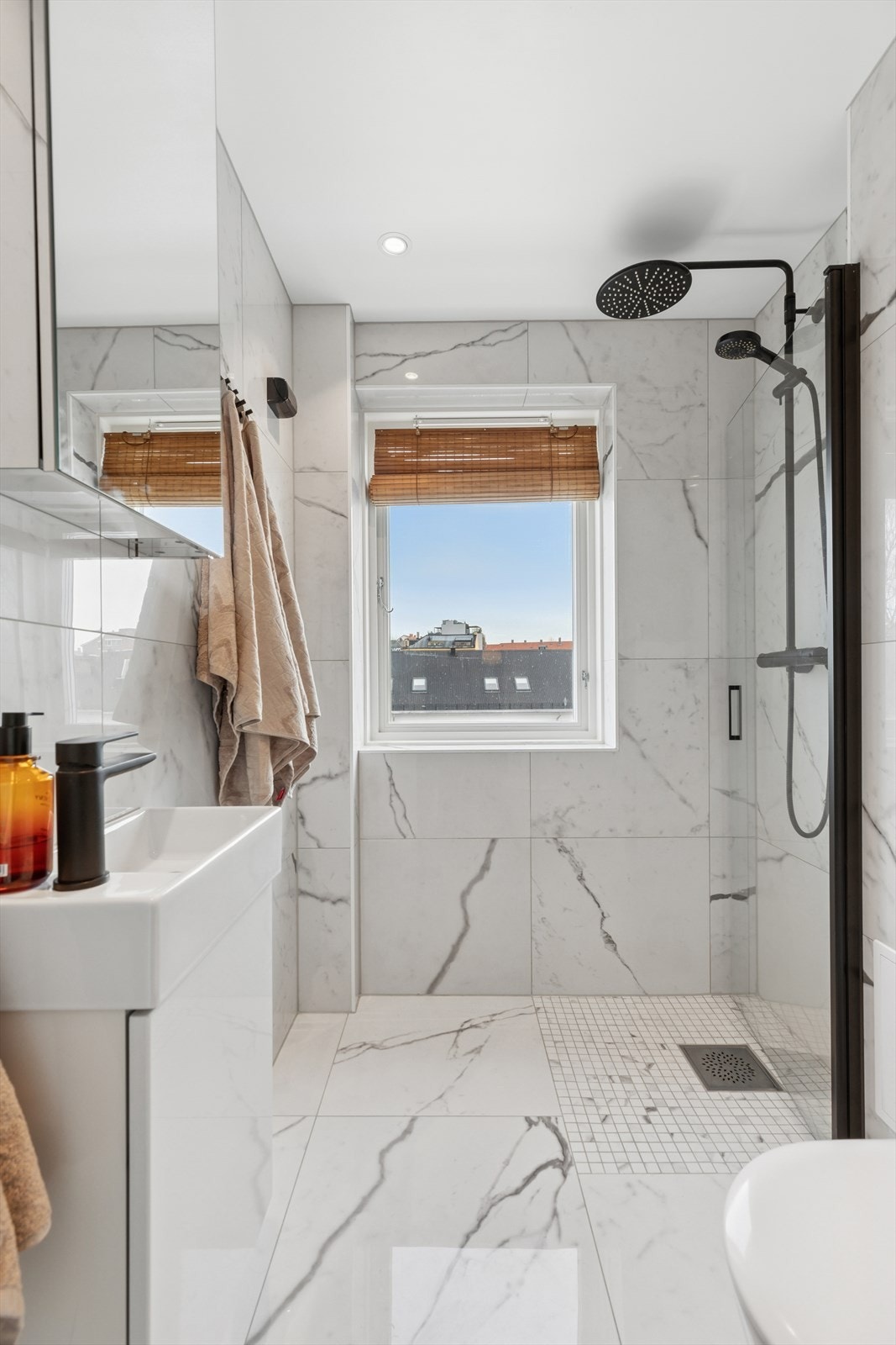 Baderommet er utstyrt med veggmontert klosett, dusj direkte på gulv med dusjvegg, nedfelt servant og et praktisk speilskap på veggen. Galleribilde