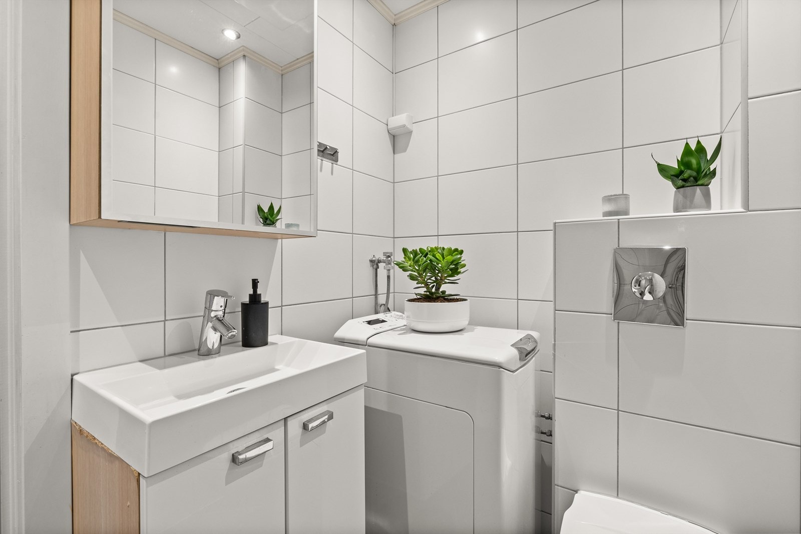 Badet har praktisk dusjhjørne, toalett, servant med innredning og opplegg for vaskemaskin (smal type) Galleribilde