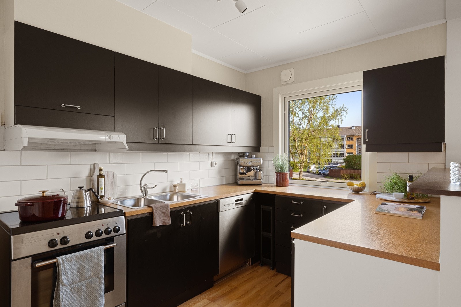 Innredningen har slette fronter og benkeplate av laminat, med fliser som backsplash over benk og over kokesonen er en ventilator installert Galleribilde