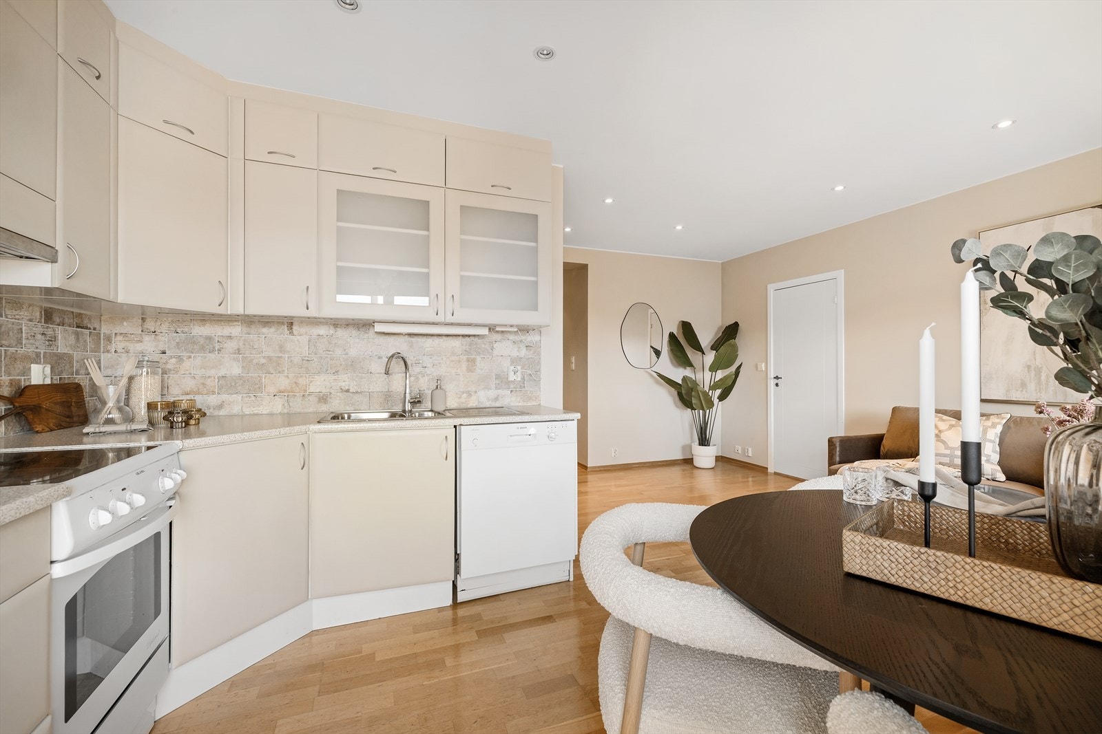 Kjøkkeninnredningen har slette, malte fronter og det er flissatt på veggen over benken. Innredningen går helt opp til taket og har en kombinasjon av skap, skuffer og vitrineskap. Galleribilde