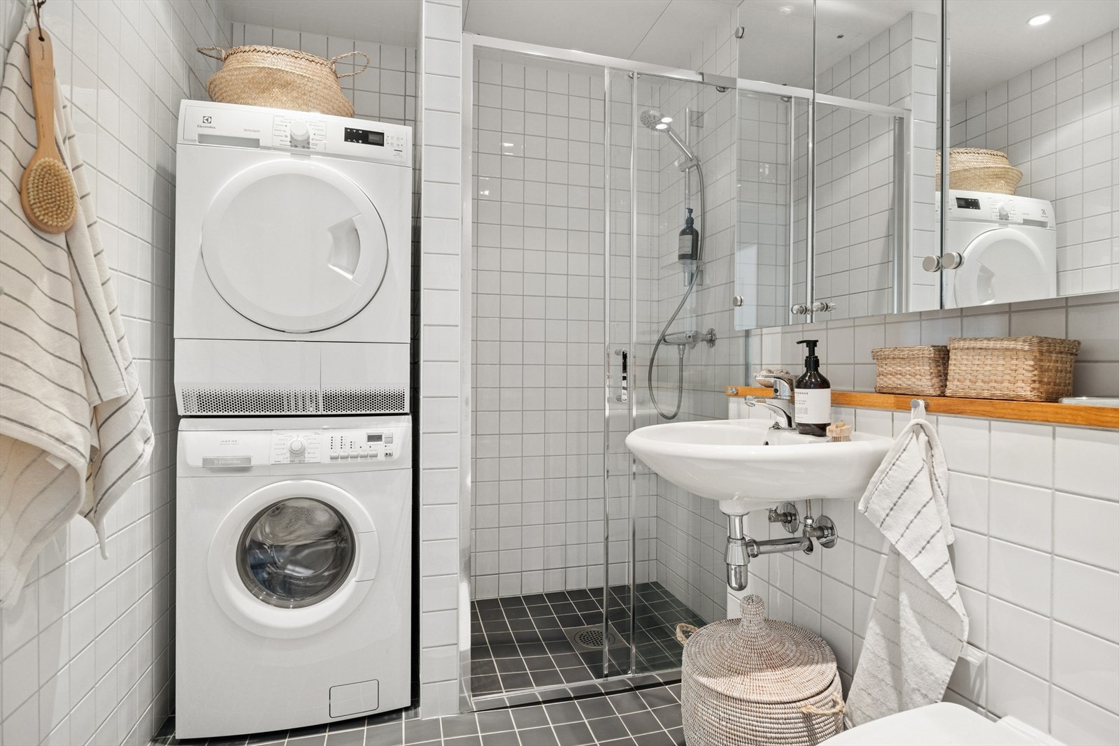 Flislagt baderom med servant, dusjhjørne, veggmontert toalett og opplegg for vaskemaskin. Galleribilde