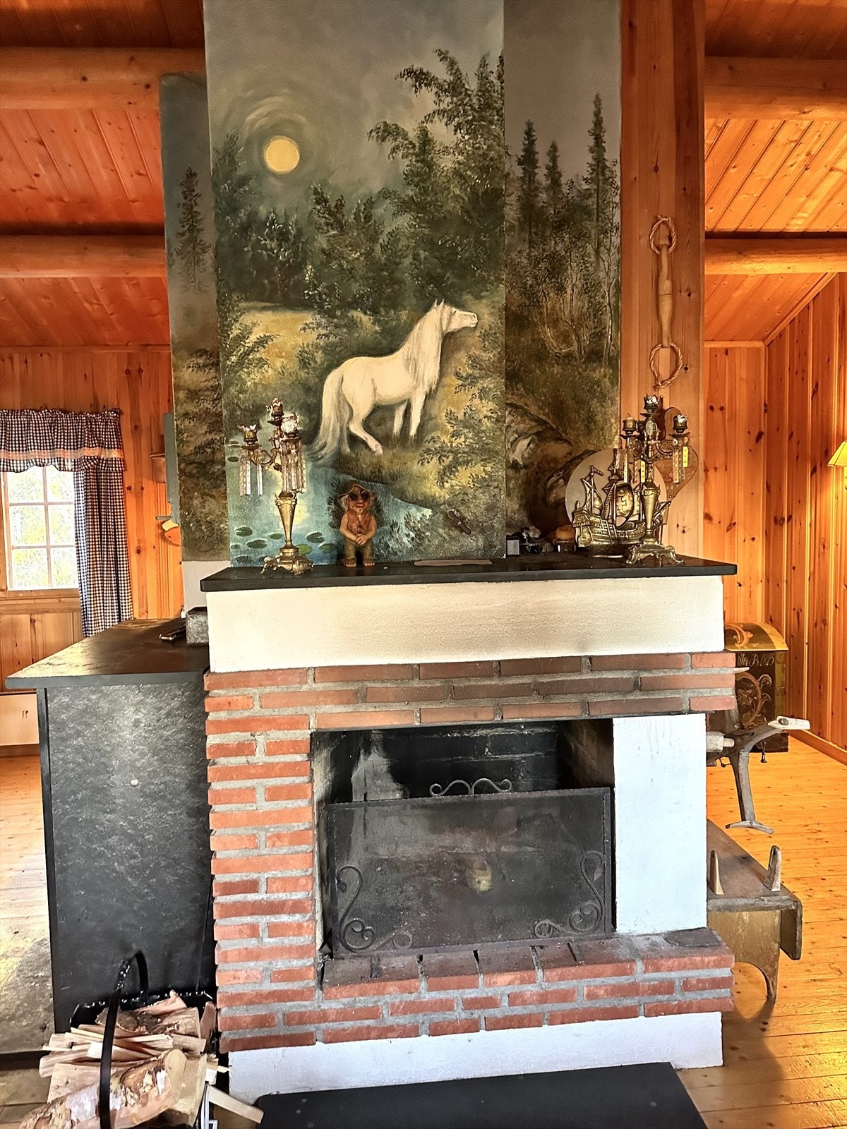 Den murte, åpne peisem med vedkamin på siden er plassert midt i rommet, og peiskappen er flott dekormalt. Galleribilde