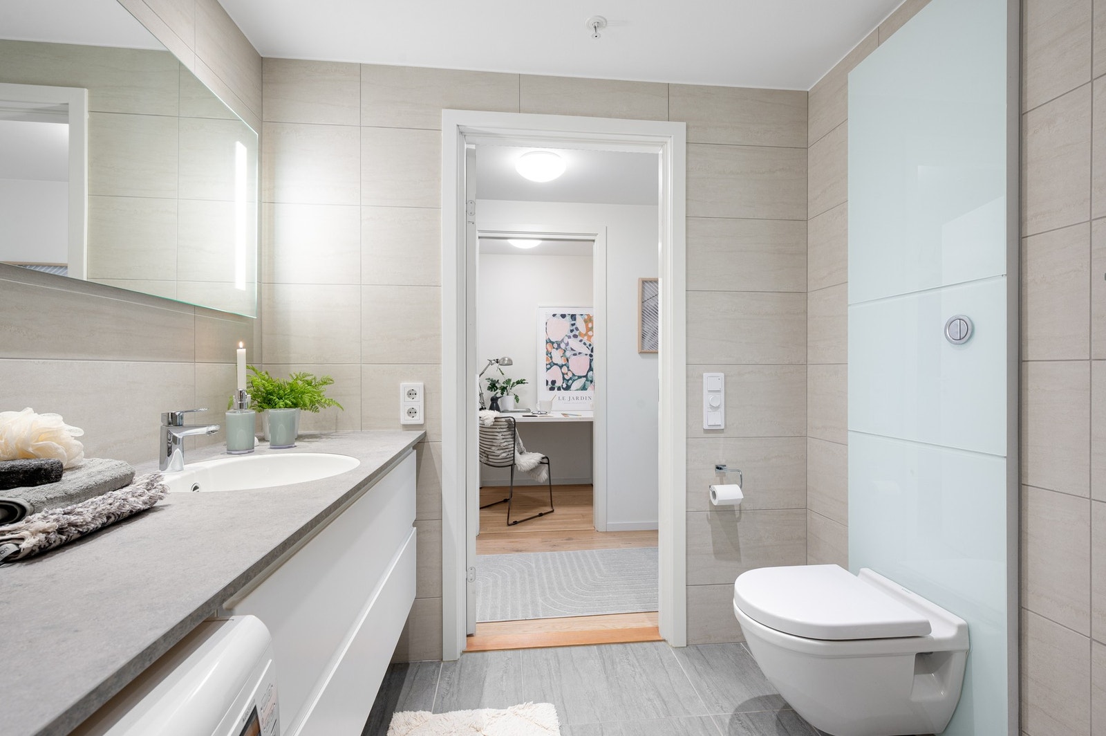 Badet er innredet med veggmontert toalett, servantinnredning, speil, dusjhjørne og elektrisk håndkletørker. Galleribilde
