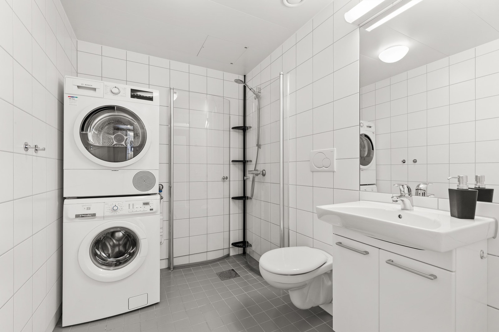 Pent flislagt bad fra byggeår med gulvvarme. Dusjhjørnet har svingbare glassdører. Det er opplegg for vaskemaskin og tørketrommel. Galleribilde