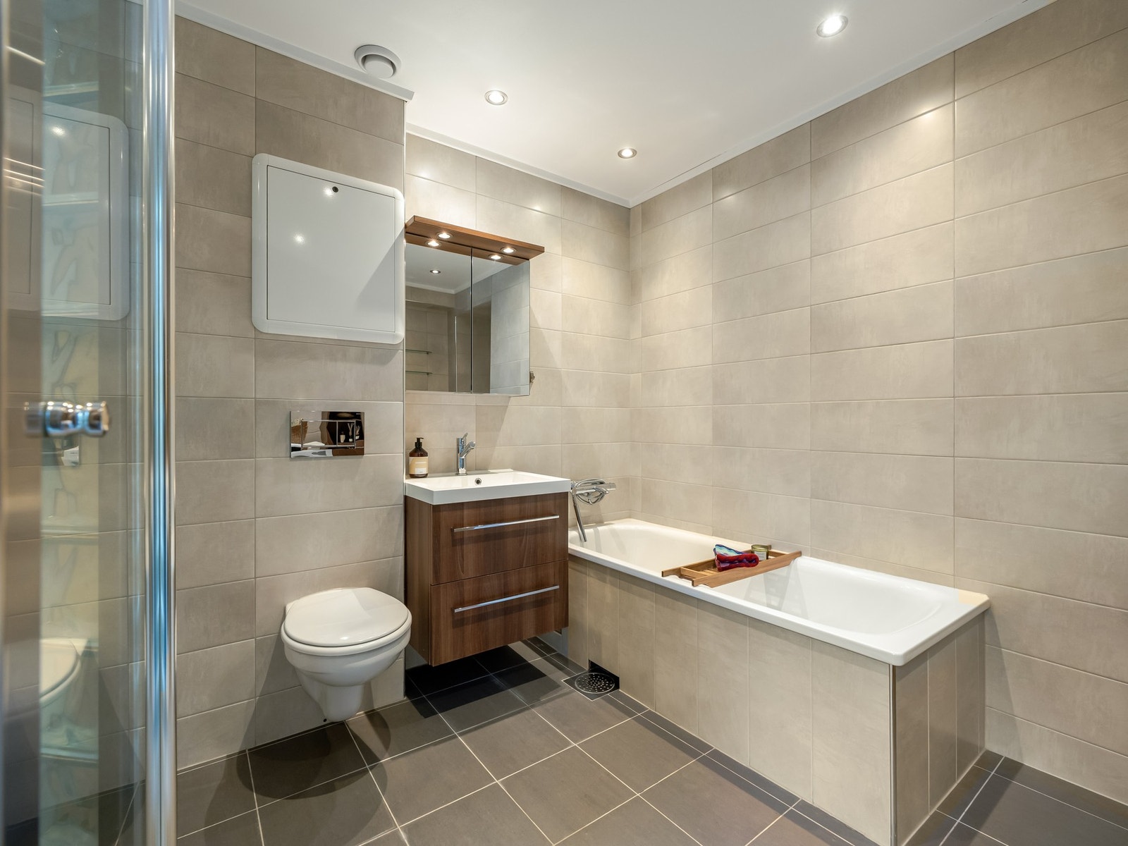 Ellers er badet innredet med både badekar og dusjhjørne, samt servant med innredning, vegghengt toalett og høyskap. Galleribilde