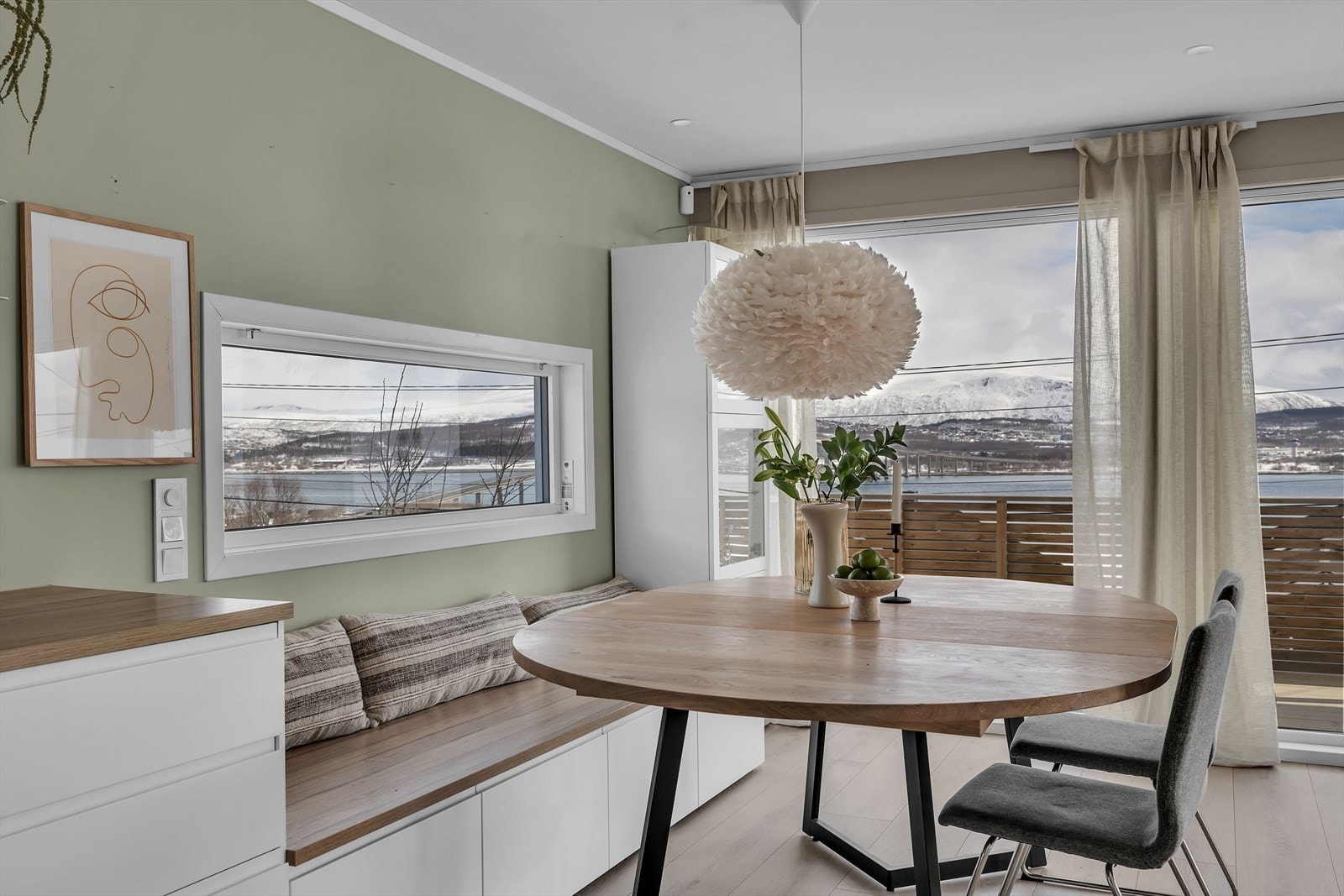 Store vindusflater slipper natur og utsikt inn i den koselige stuen som er i åpen løsning med kjøkkenet. Galleribilde