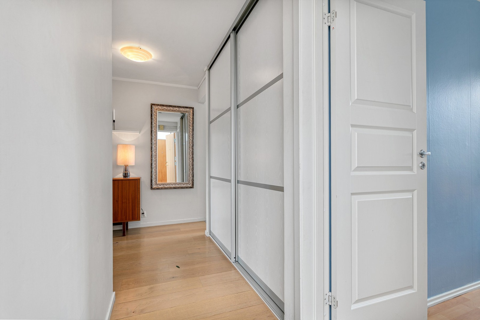 Entréen er utstyrt med oppbevaringsmøbel og en pent integrert skyvedørsgarderobe med hvite fronter Galleribilde