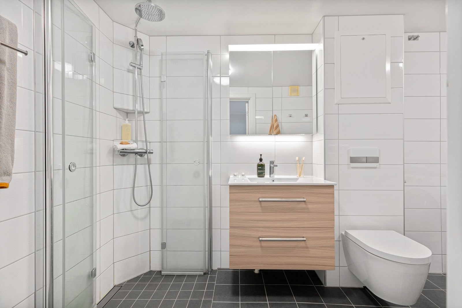 Et dusjhjørne har foldede glassdører og dusjing direkte på gulv. Badet har varmekabler i gulv Galleribilde