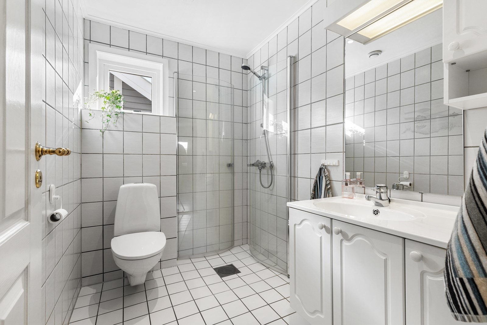 Bad med fliser på gulv og vegger. Badet har toalett, servant med skap og dusjnisje med innfellbare glassdører. Varmekabler i gulv. Galleribilde