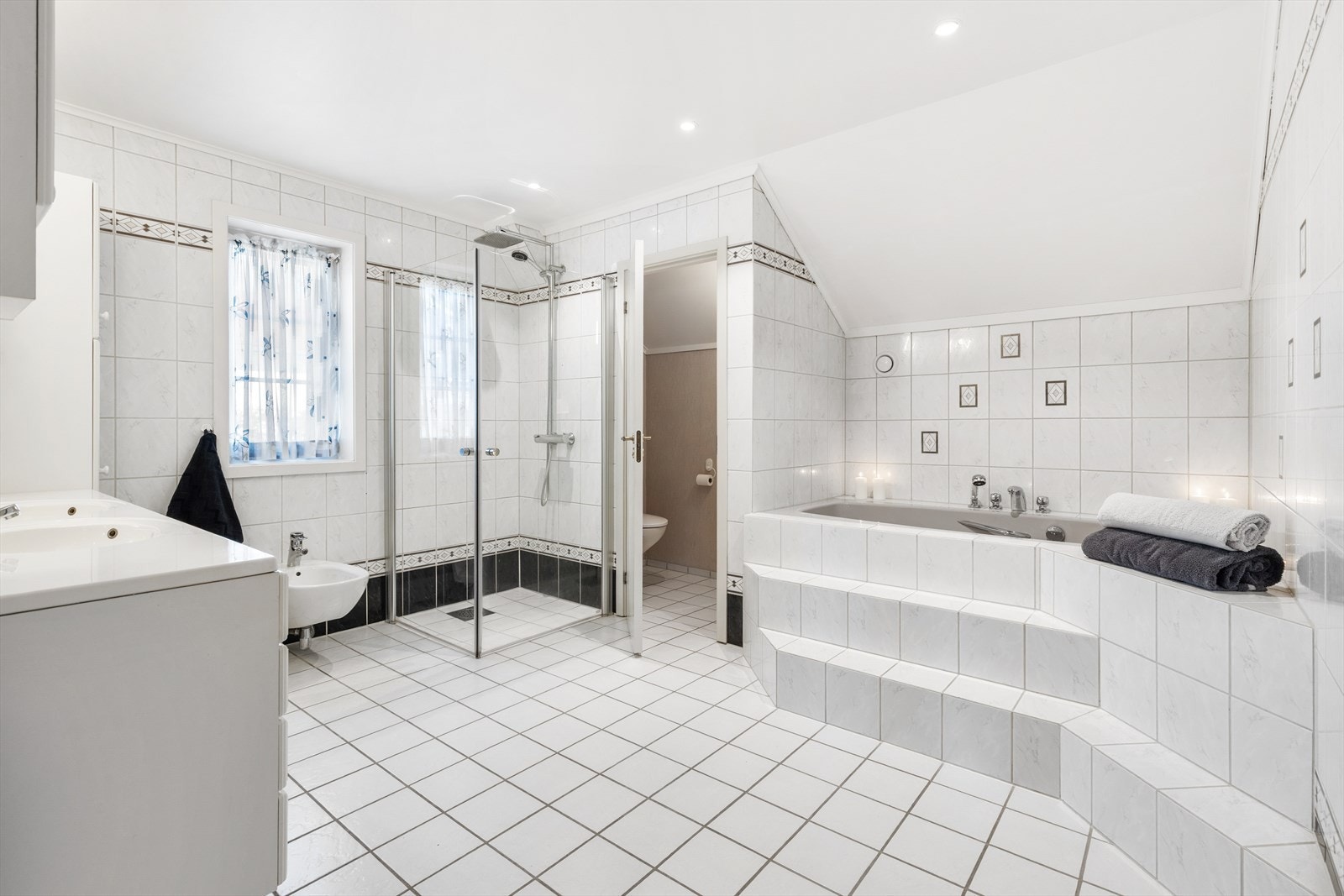 Badet er innredet med bidé, dobbelservant med skuffer og skap, badekar, wc og dusjnisje med innfellbare glassdører. Galleribilde
