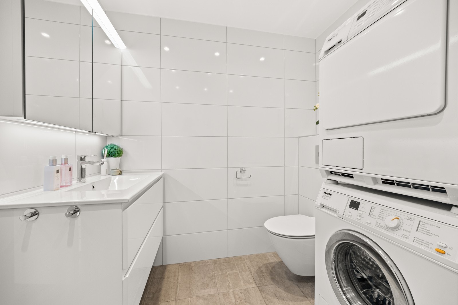 Det er servant i innredning, vegghengt toalett, lekkert og romslig dusjhjørne og opplegg for vaskemaskin og tørketrommel Galleribilde