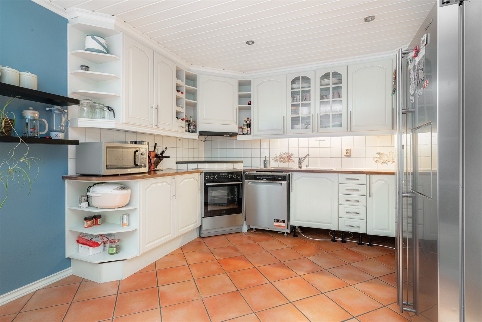 Kjøkkenet har en hvit, takhøy innredning med profilerte fronter og noe glasskap, laminat benkeplate og flis over kjøkkenbenk. Det er ventilator med avtrekk ut og avsatt plass til komfyr, oppvaskmaskin og kjøleskap. Galleribilde