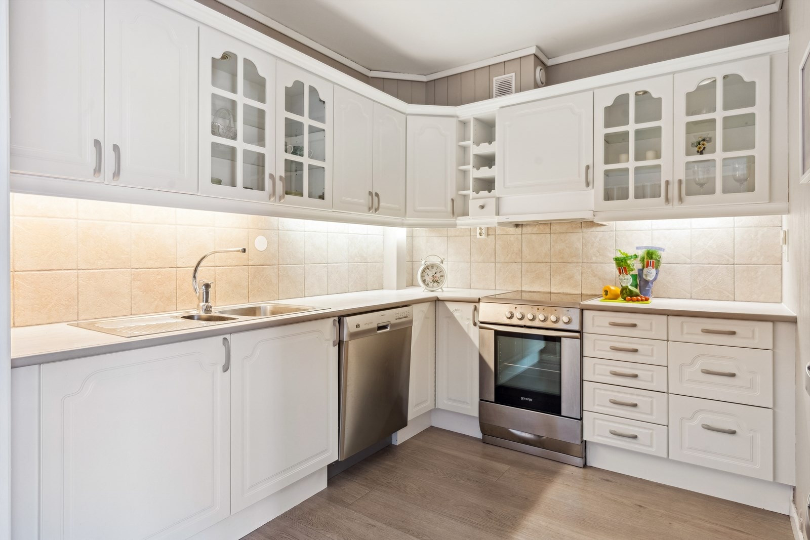 Sigdal kjøkken med profilerte fronter, hvorav 4 fronter er av glass, benkeplaten er av laminat, fliser på vegg over benk og stålvask Galleribilde