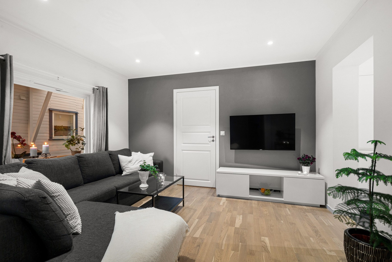 Stuen har nøytrale farger med eikefarget parkettgulv og hvite vegger i fin kontrast til en gråmalt aksentvegg. Galleribilde