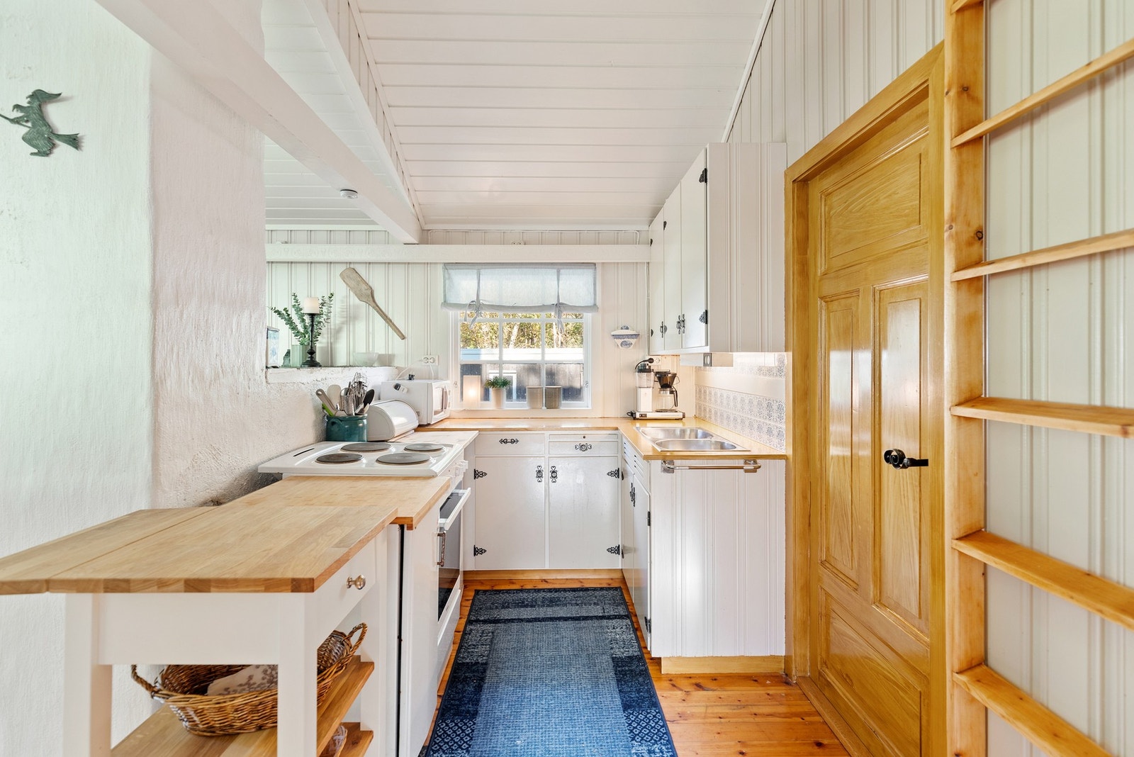 Kjøkkenet har plassbygget innredning i hvite, profilerte fronter. Innredningen inneholder videre laminat benkeplate med flis mot overskap, oppvaskkum, utslagsvask og komfyr. Galleribilde