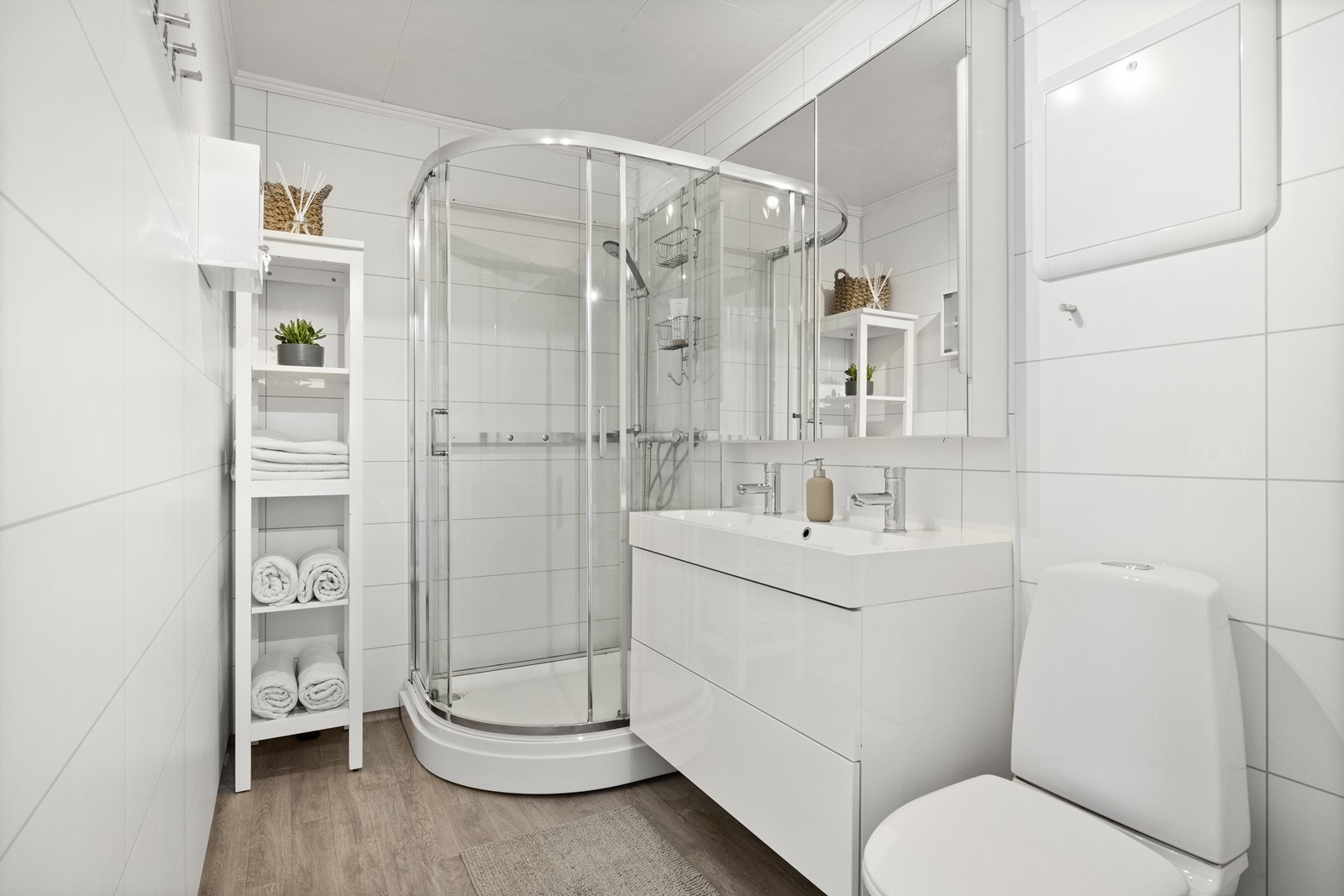 Pent baderom med våtromsplater på vegg og vinylbelegg på gulv. Badet er utstyrt med toalett, servant med skuffer og dusjkabinett. Galleribilde