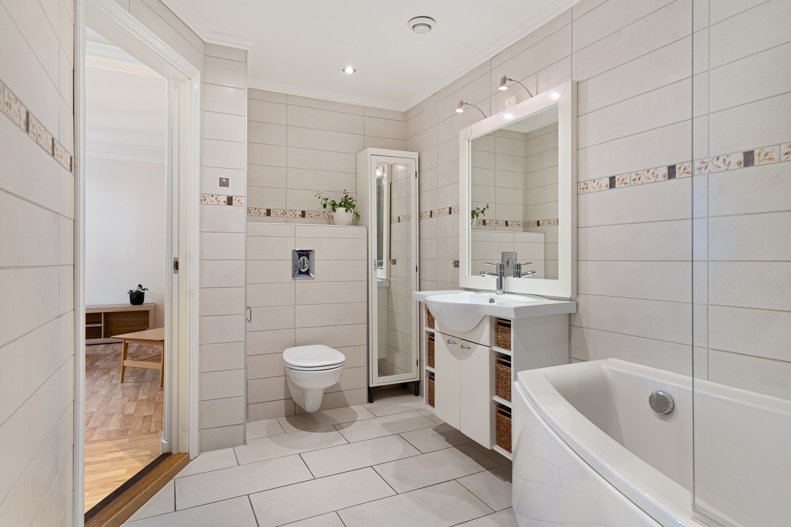 Stort bad med badekar med dusj, vegghengt toalett, servant med skap og praktisk nisje til vaskemaskine og tørketrommel Galleribilde