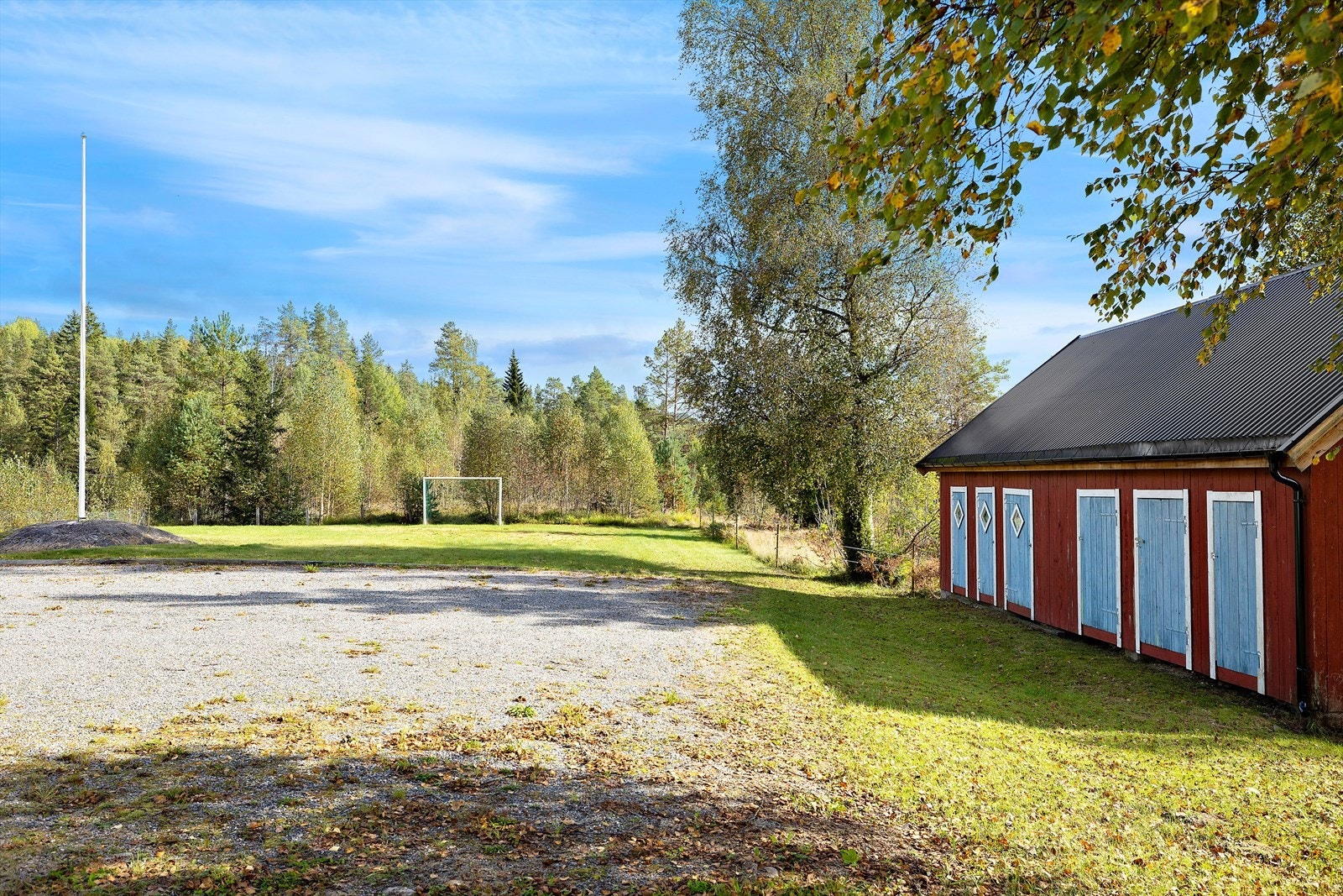Stor tomt med gruset parkeringsplass og en liten fotballbane Galleribilde