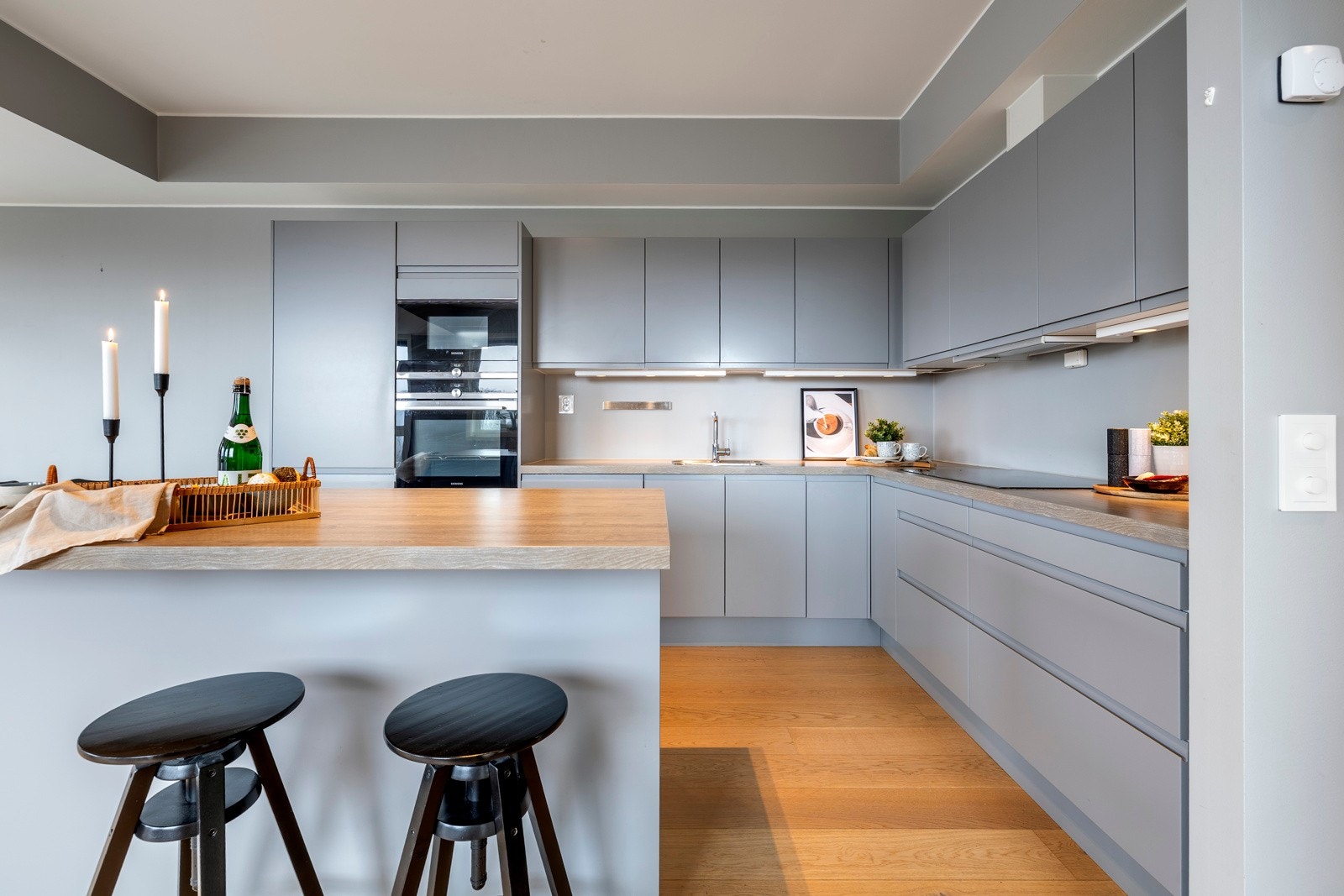 Benkeplaten er i eikelaminat med underlimt vaskekum og bred, nedfelt koketopp. Stekeovn, mikrobølgeovn, oppvaskmaskin, kjøl/frys og ventilator er også integrert. Kjøkkensonen markeres av ekstra takhøyde og får godt lys fra stuevinduene, downlights m.m. Galleribilde