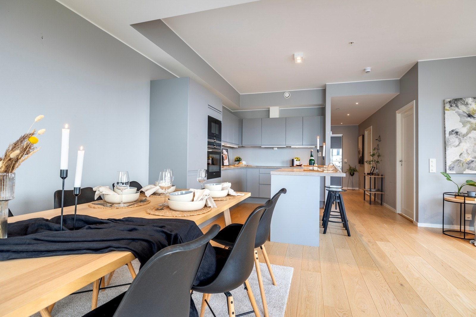 Kjøkkenet er plassert i en hendig L-form, innerst i stuen, pluss en stor øy med barløsningen i overgangen til stuesonen. Innredningen har glatte, grå fronter, nært opp til veggfargen, slik at den visuelt nærmest går i ett med bakgrunnen. Galleribilde