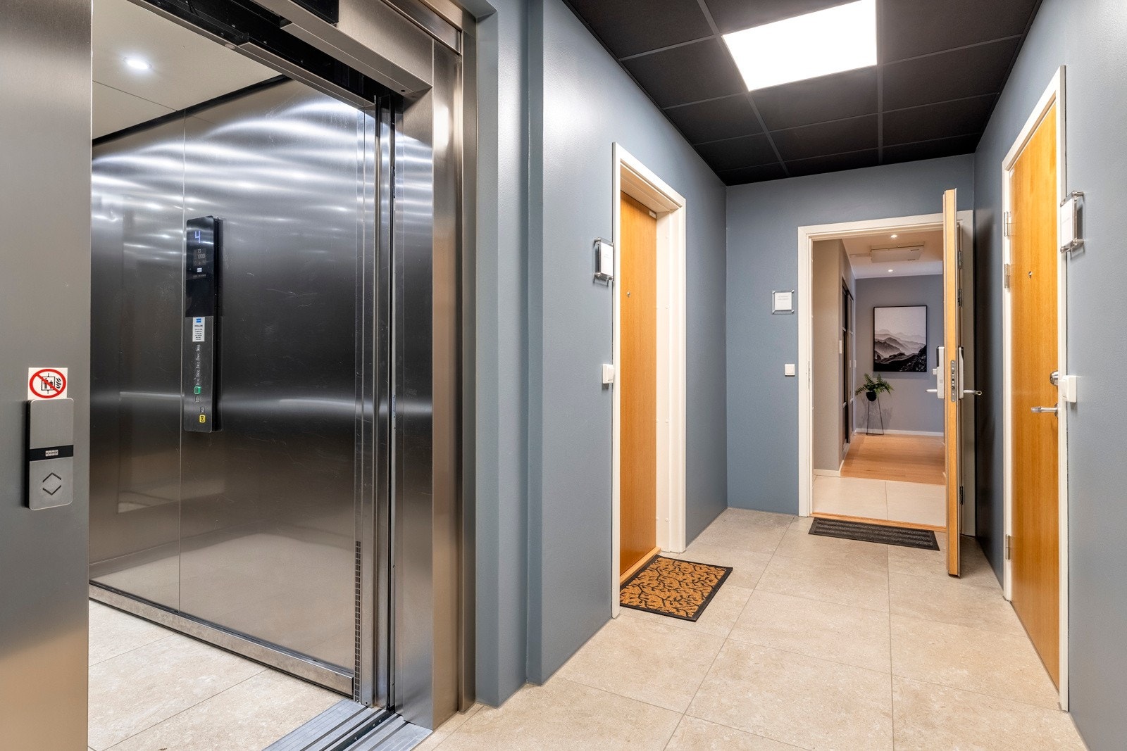 Bygget har heis til alle etasjene og innbydende oppganger med flislagt gulv. Leilighetens ytterdør er utstyrt med smart kodelås og entreen er pent utført med lyse fliser på gulvet, glatte, gråmalte veggflater og listefri himling med downlights. Galleribilde