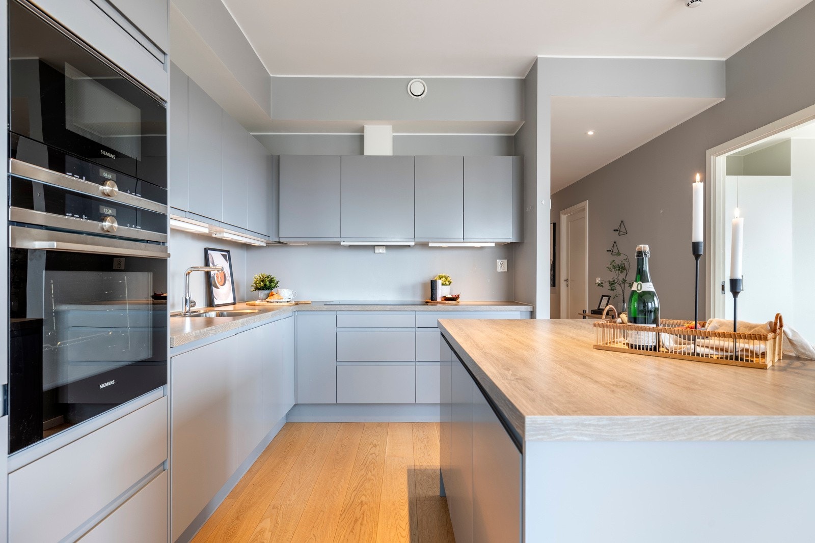 Benkeplaten er i eikelaminat med underlimt vaskekum og bred, nedfelt koketopp. Stekeovn, mikrobølgeovn, oppvaskmaskin, kjøl/frys og ventilator er også integrert. Kjøkkensonen markeres av ekstra takhøyde og får godt lys fra stuevinduene, downlights m.m. Galleribilde