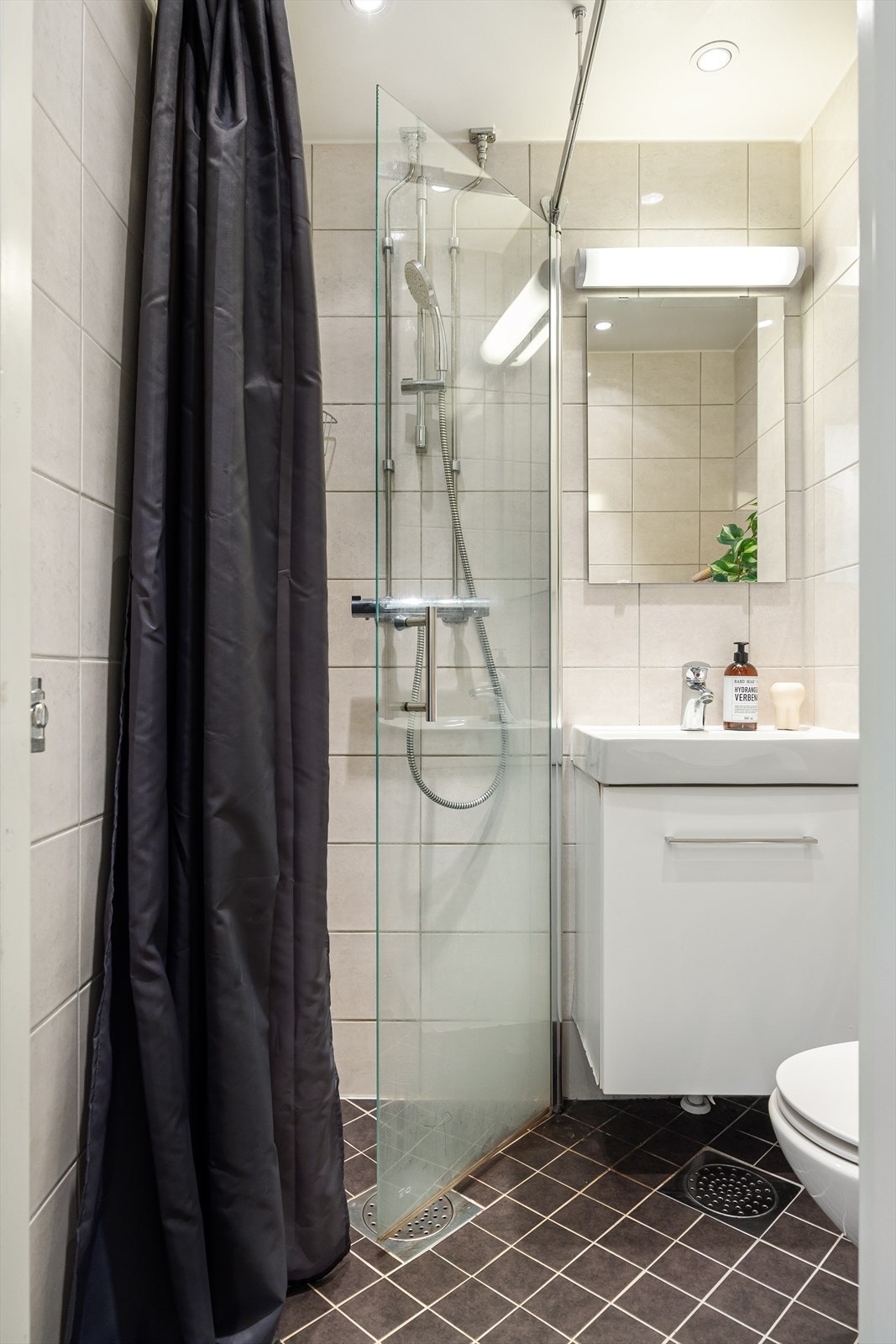 Badet består av veggmontert WC, dusjplass med dusjvegg og forheng og servant med ettgreps blandebatteri i innredning. Galleribilde