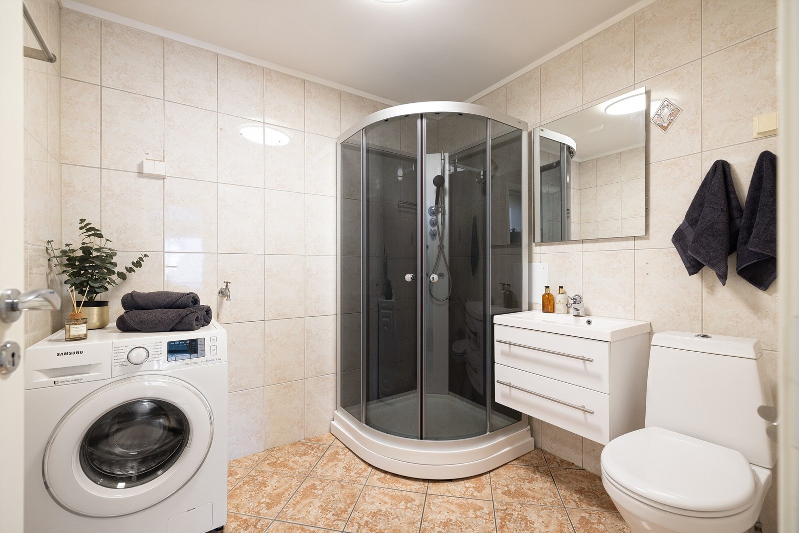 Innredning og garnityr på bad inneholder gulvstående toalett, dusjkabinett og baderomsinnredning med servant med ettgreps blandebatteri, skuffer og vegghengt speil. Det er opplegg for vaskemaskin. Galleribilde